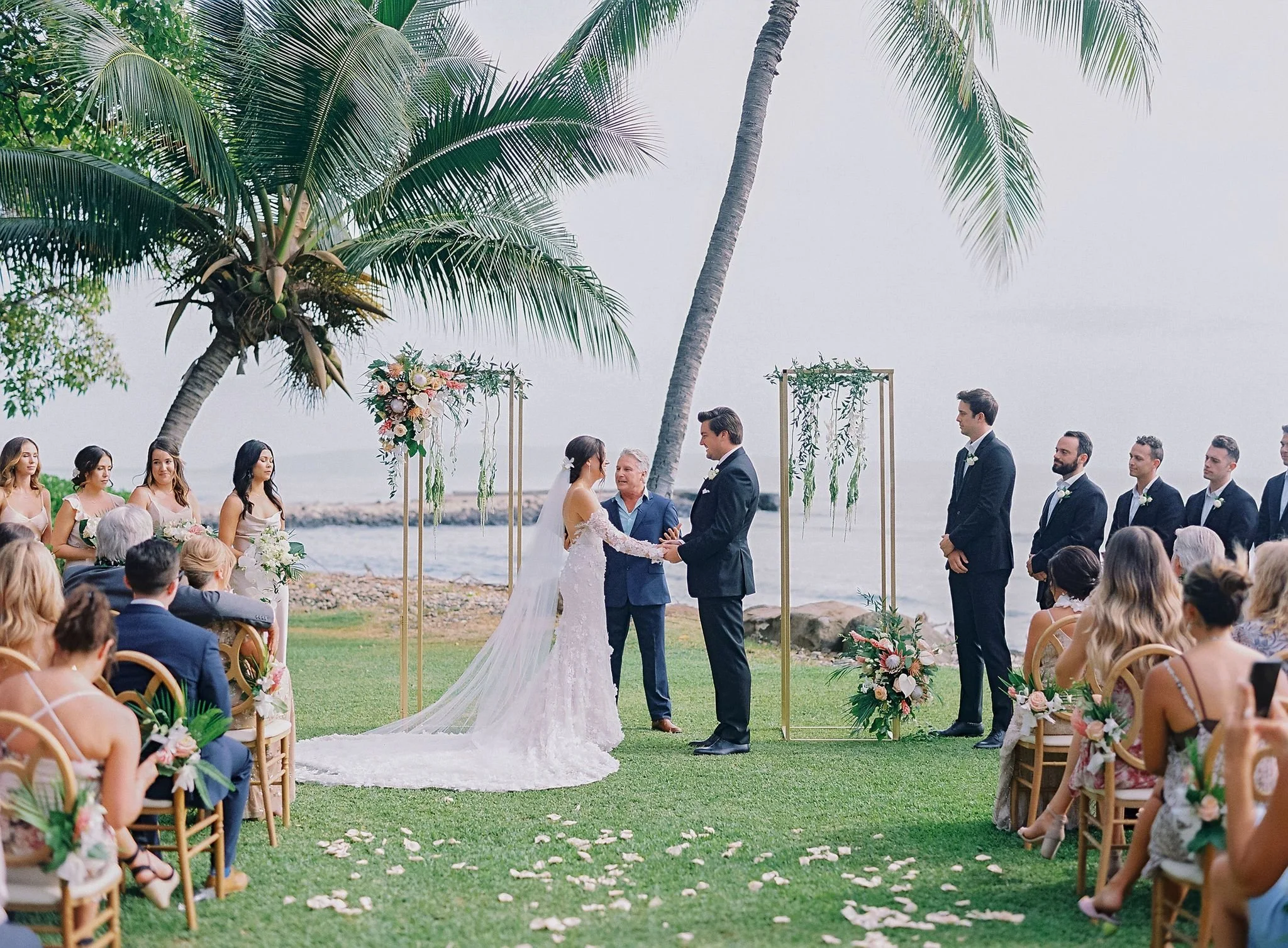 A bride and groom getting married on green grass with an ocean backdrop.