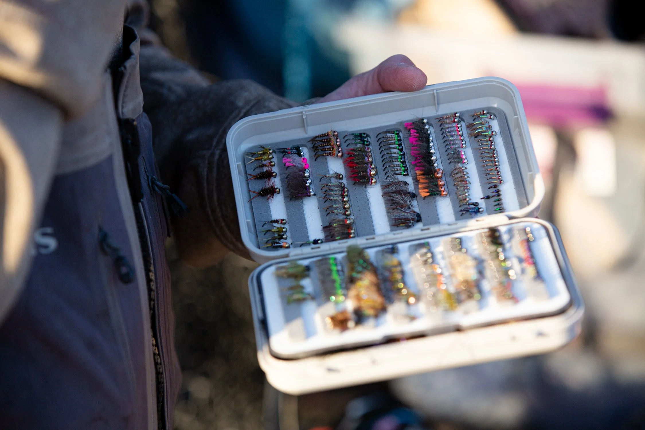 Close-up of a person holding a plastic case filled with colorful fishing flies used for fly fishing.