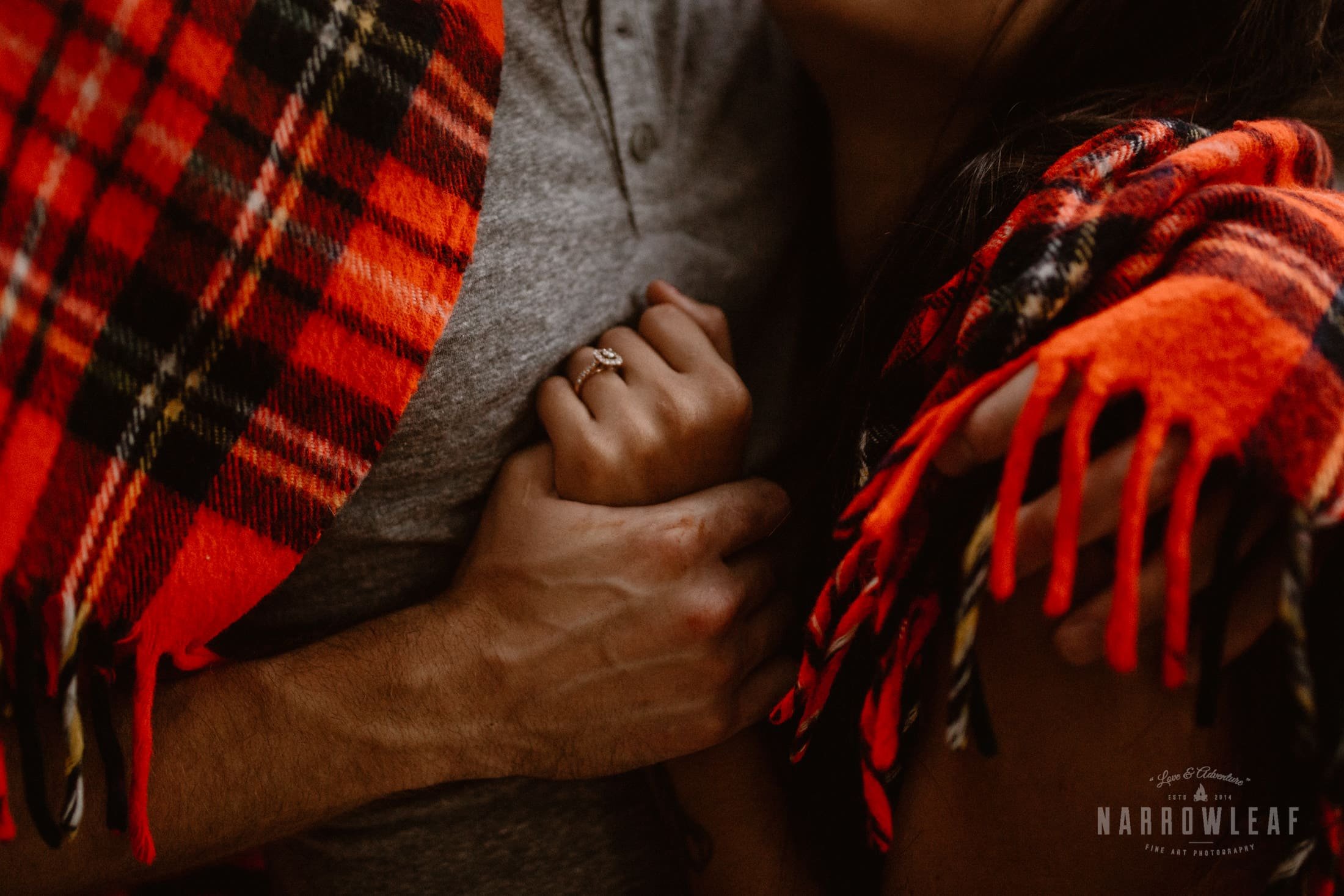 Engaged couple cuddling in a plaid blanket.jpg