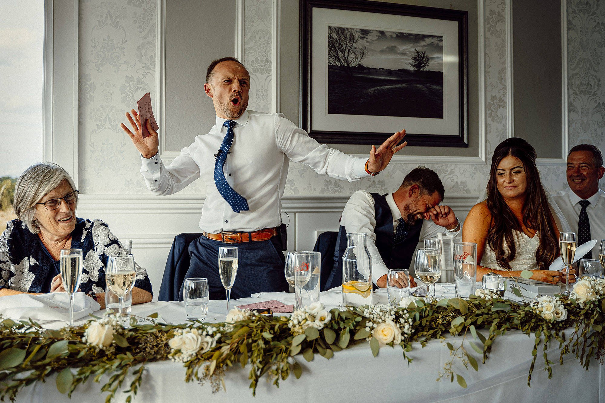 Wedding reception speech with people laughing at the best man whose waving his arms in some kind of dance move.