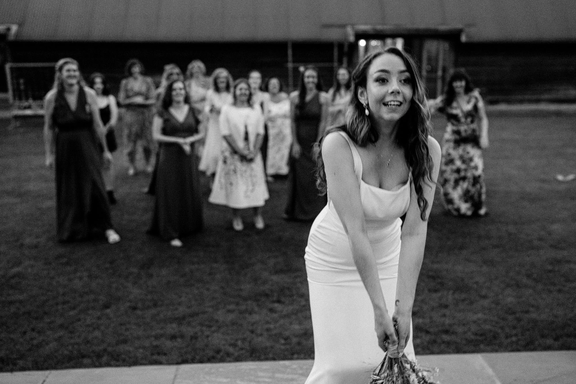 Black & White photo of a bride about to toss her bouquet with her friends waiting in the background to catch it.