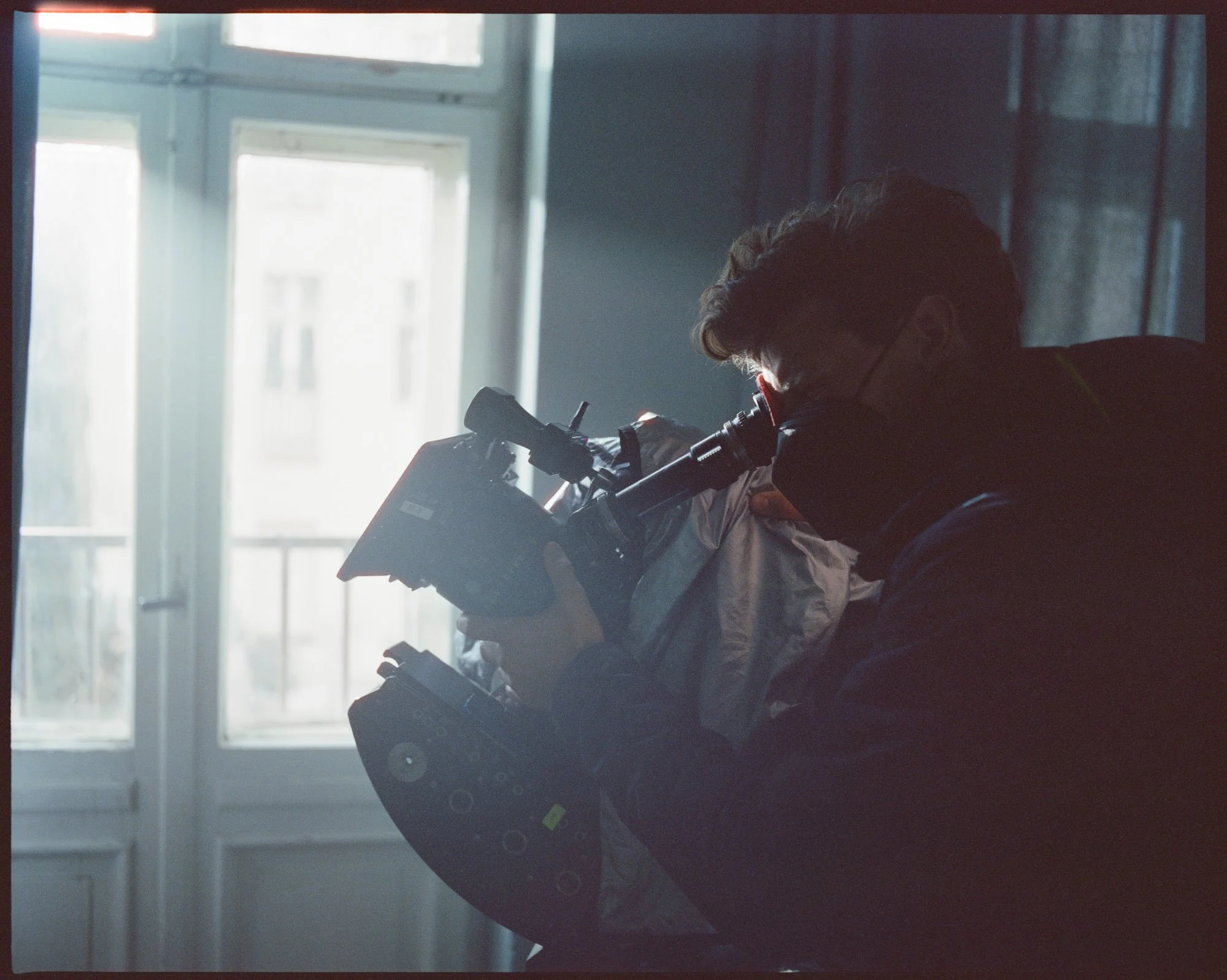 A person looking through a microscope indoors near a window with daylight coming through.
