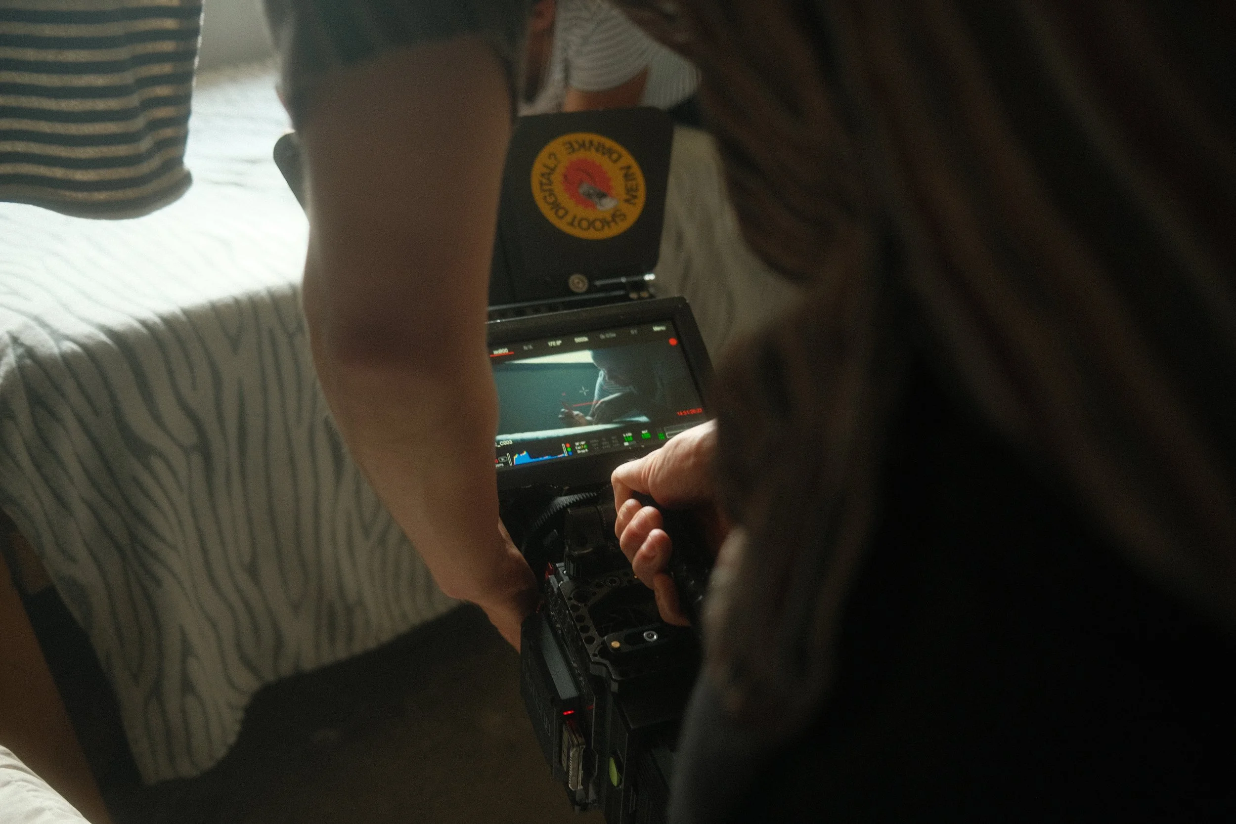 Person recording a video or taking a photo with a professional camera, with the camera's screen showing a silhouette of a person sitting at a table.
