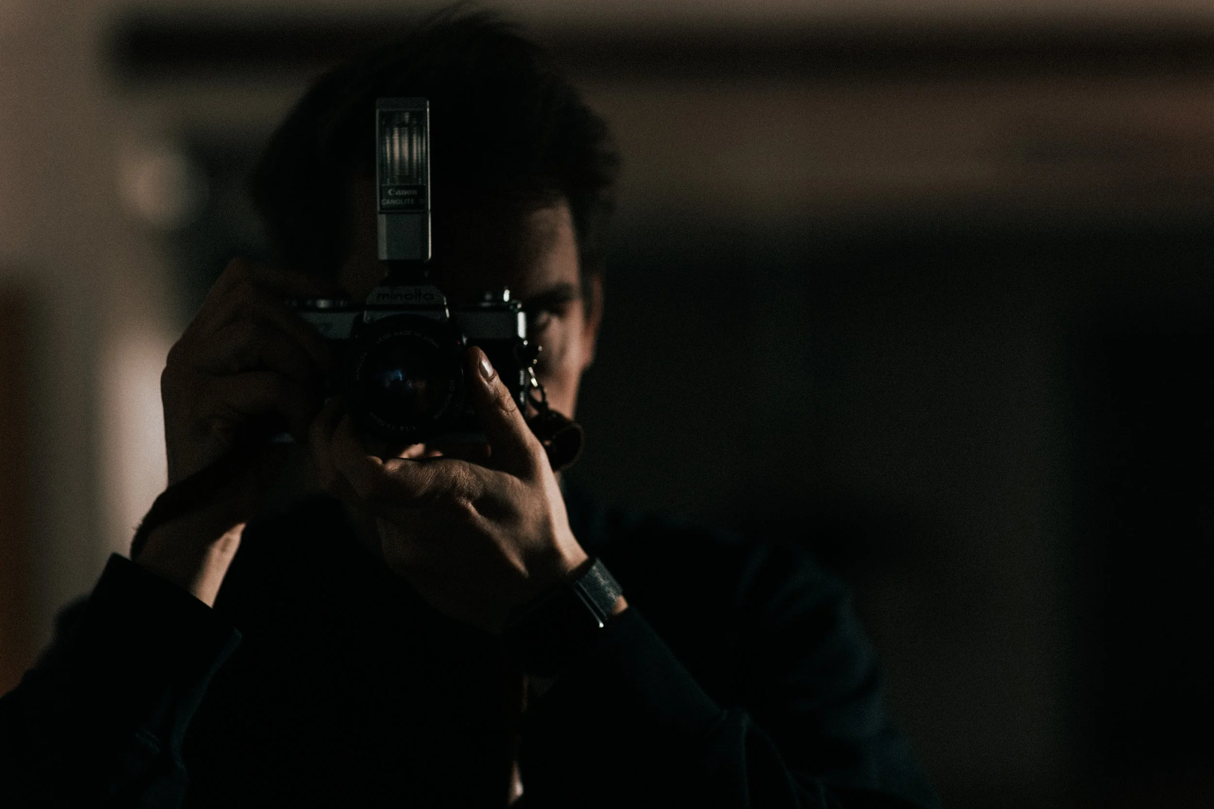 Person taking a photograph with a Canon camera and external flash in a dimly lit environment.