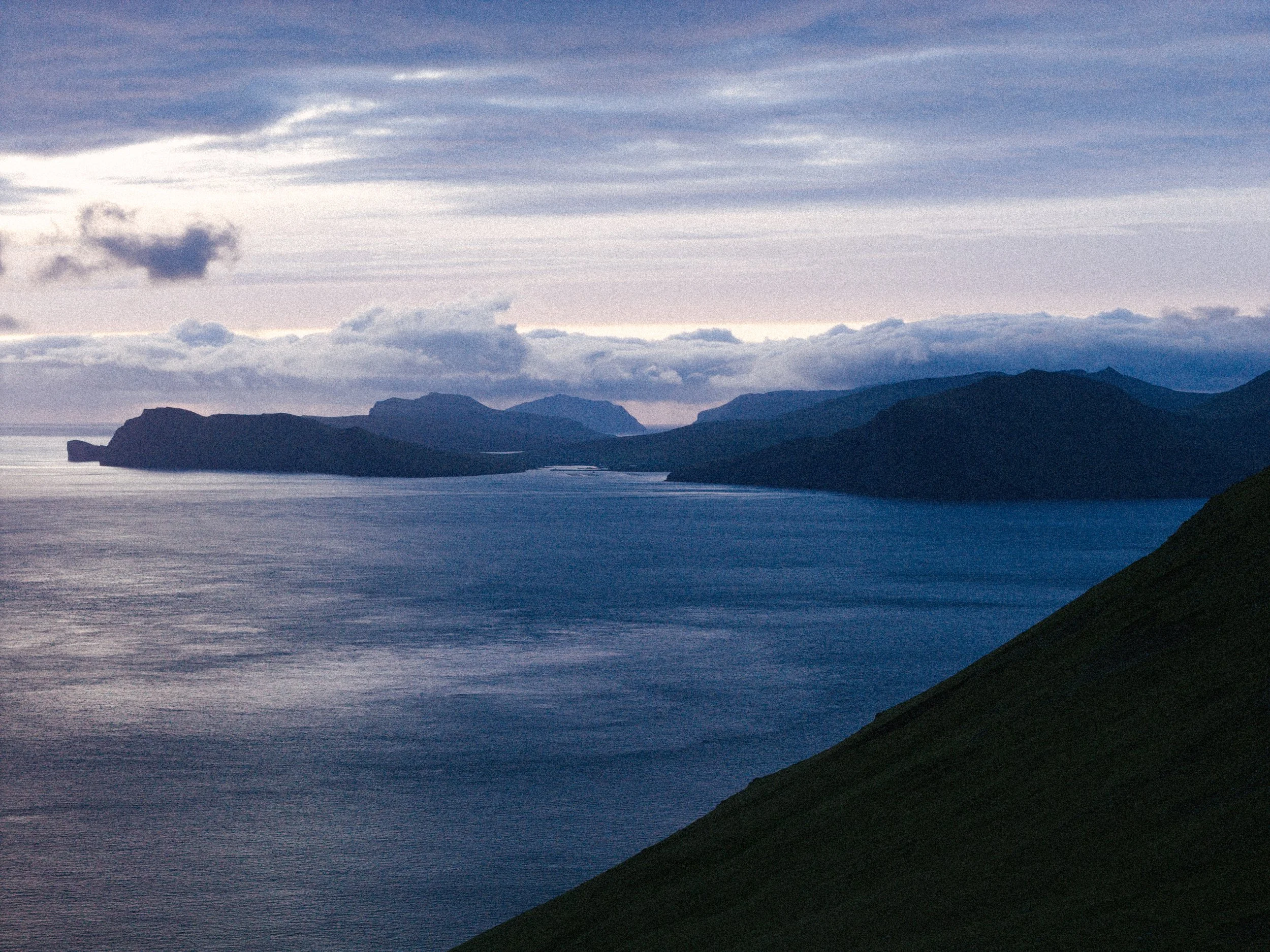 Scenic view of a body of water with multiple islands and mountains in the background, under a cloudy sky, near sunset or sunrise.