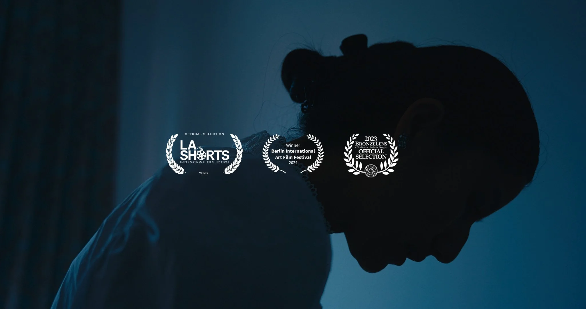 Silhouette of a person with glasses, head bowed, against a dark blue background, with three film festival laurels overlayed and awards for LA Shorts, Berlin International Art Film Festival, and Brozenlens Film Festival.