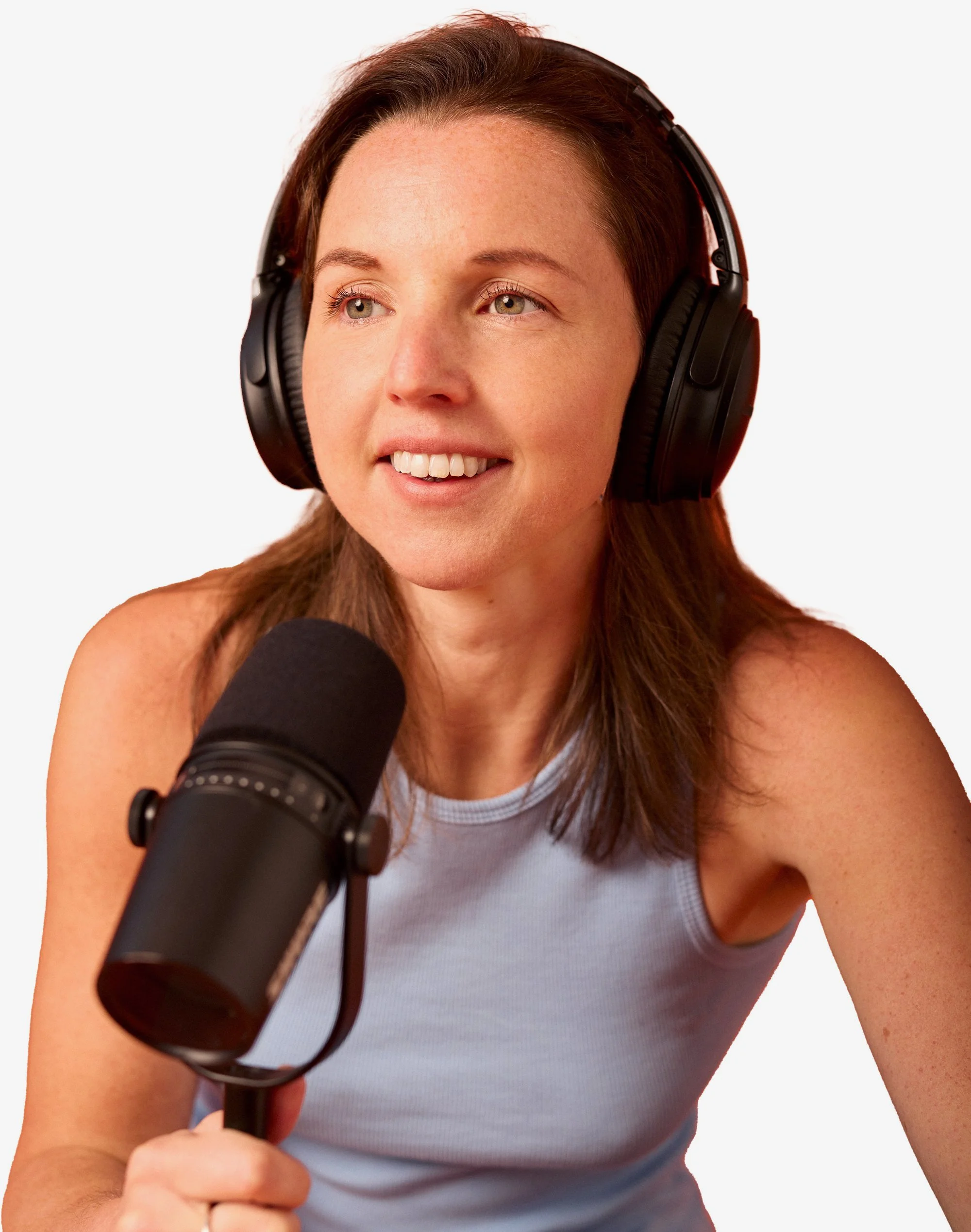 A woman with brown hair wearing headphones, holding a microphone, smiling and looking to her side.