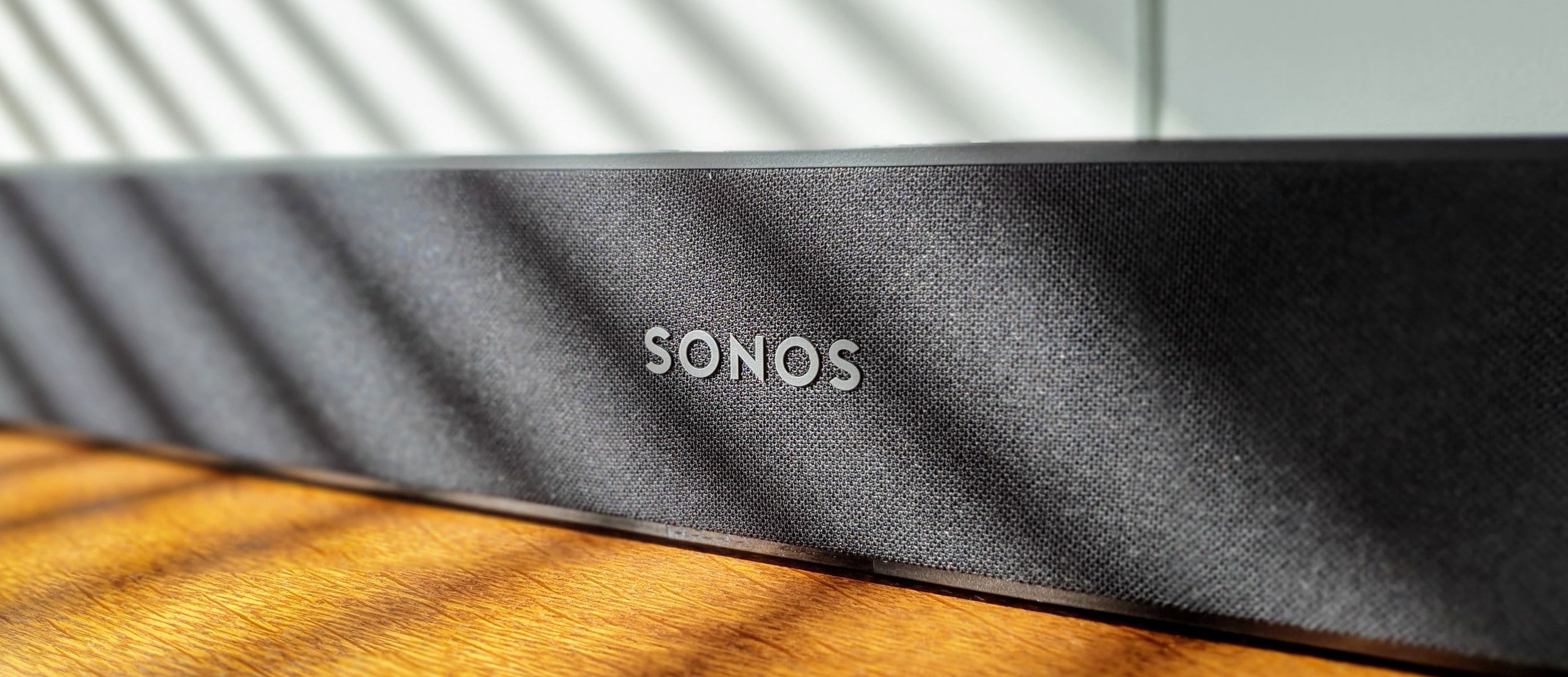 Close-up of a black Sonos speaker with a textured grille, placed on a wooden surface.