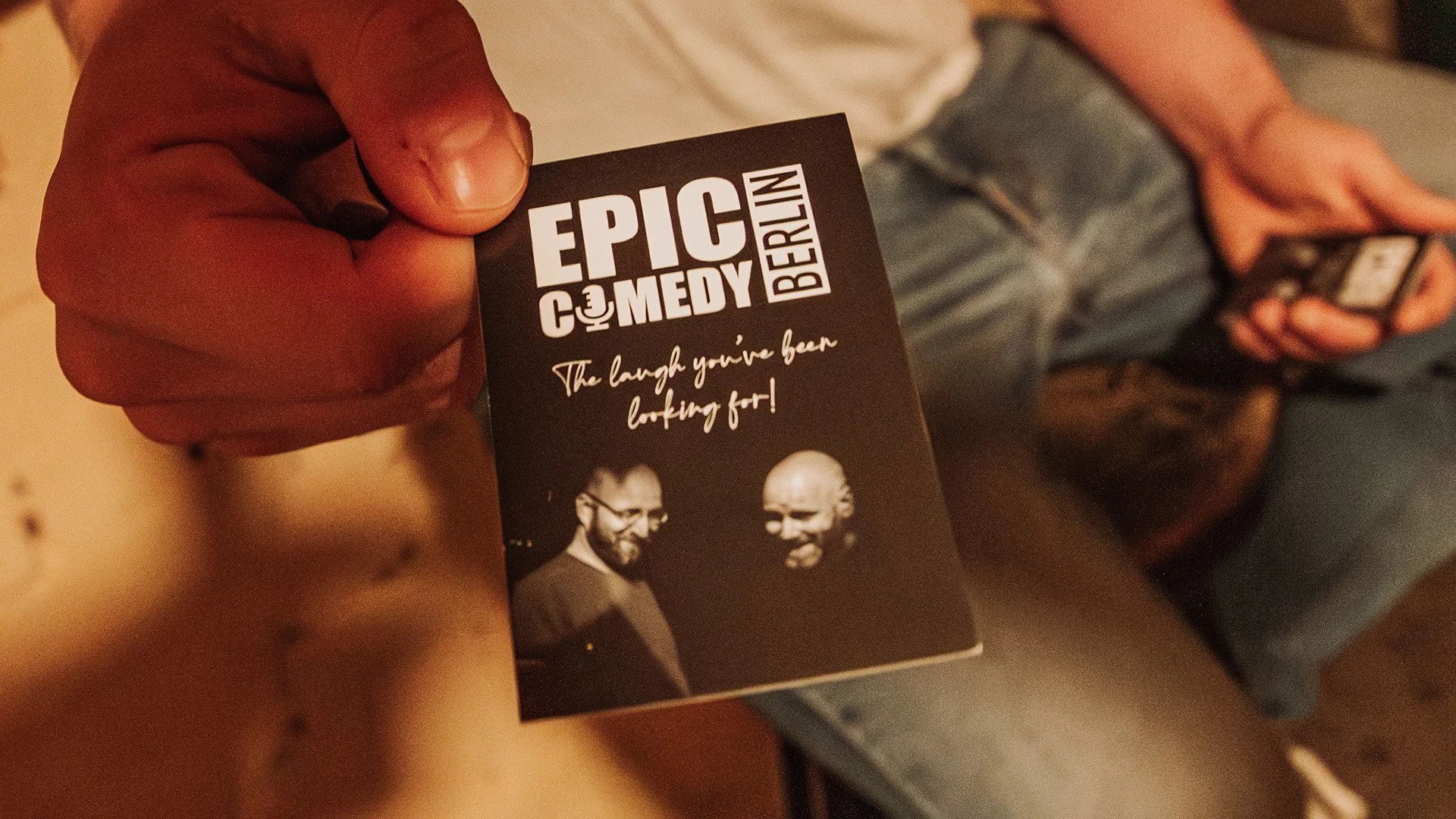 A hand holding an Epic Comedy Berlin card with Ori Halevy and Brendan Hickey: “The laugh you’ve been looking for!”