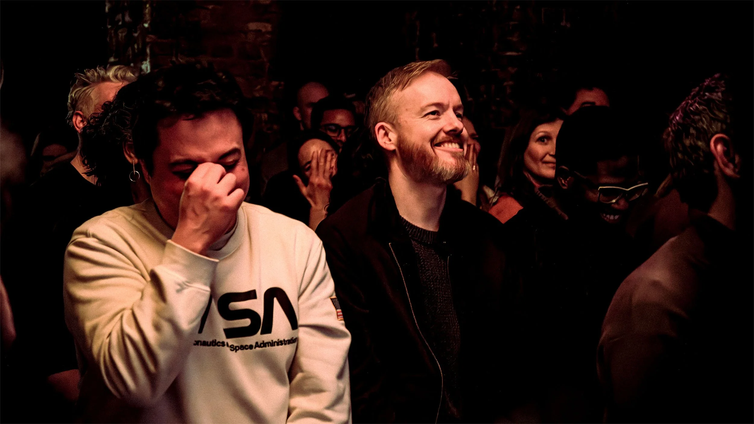 Audience members laughing during a live Epic Comedy Berlin English comedy show in Berlin, one covering his face mid-laugh