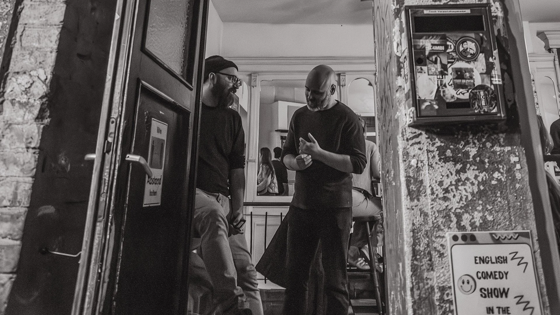 Black-and-white photo of comedians Ori Halevy and Brendan Hickey talking in a bar doorway in Berlin