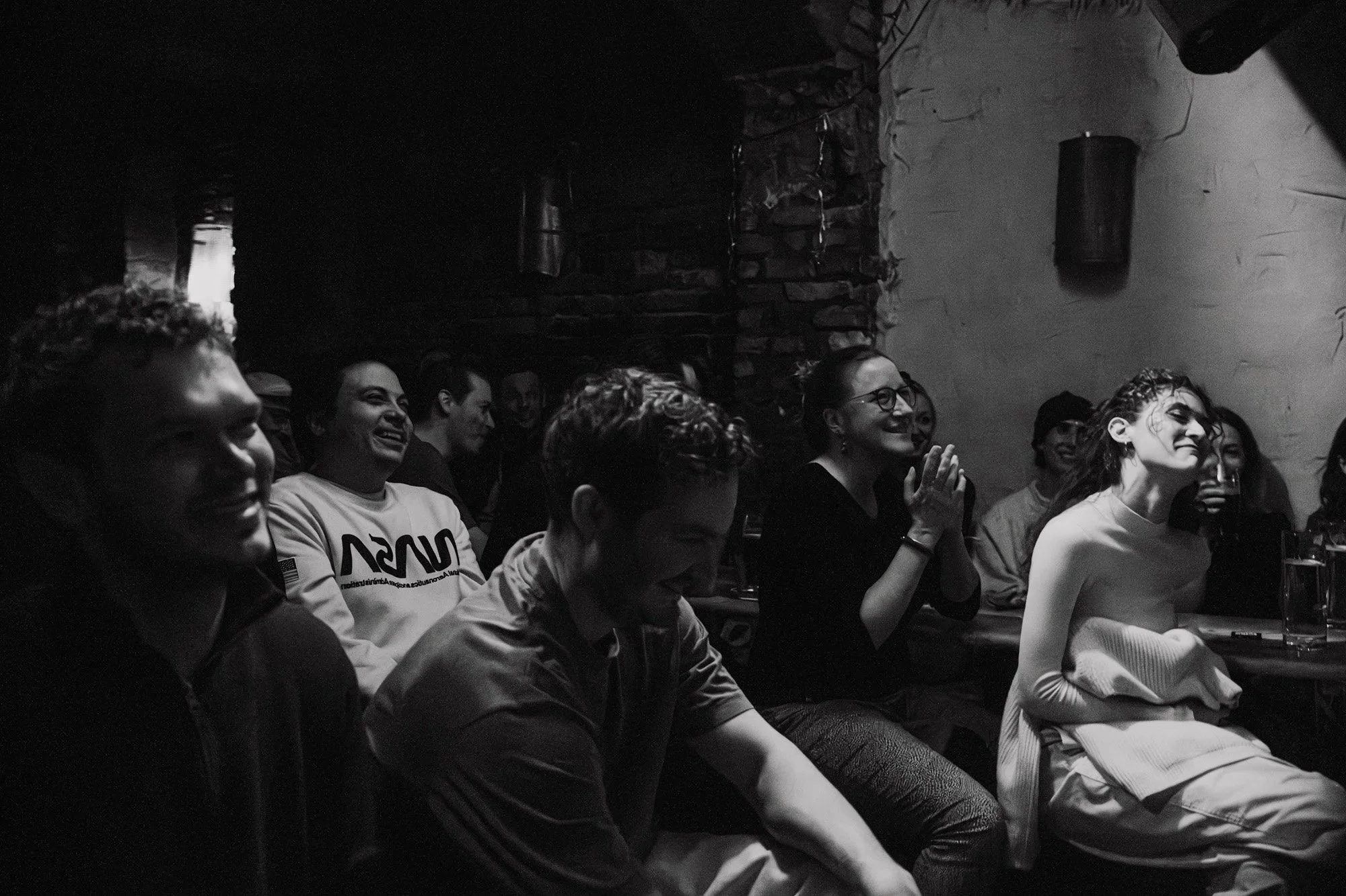 Black-and-white photo of a laughing audience in a brick-walled comedy room in Berlin