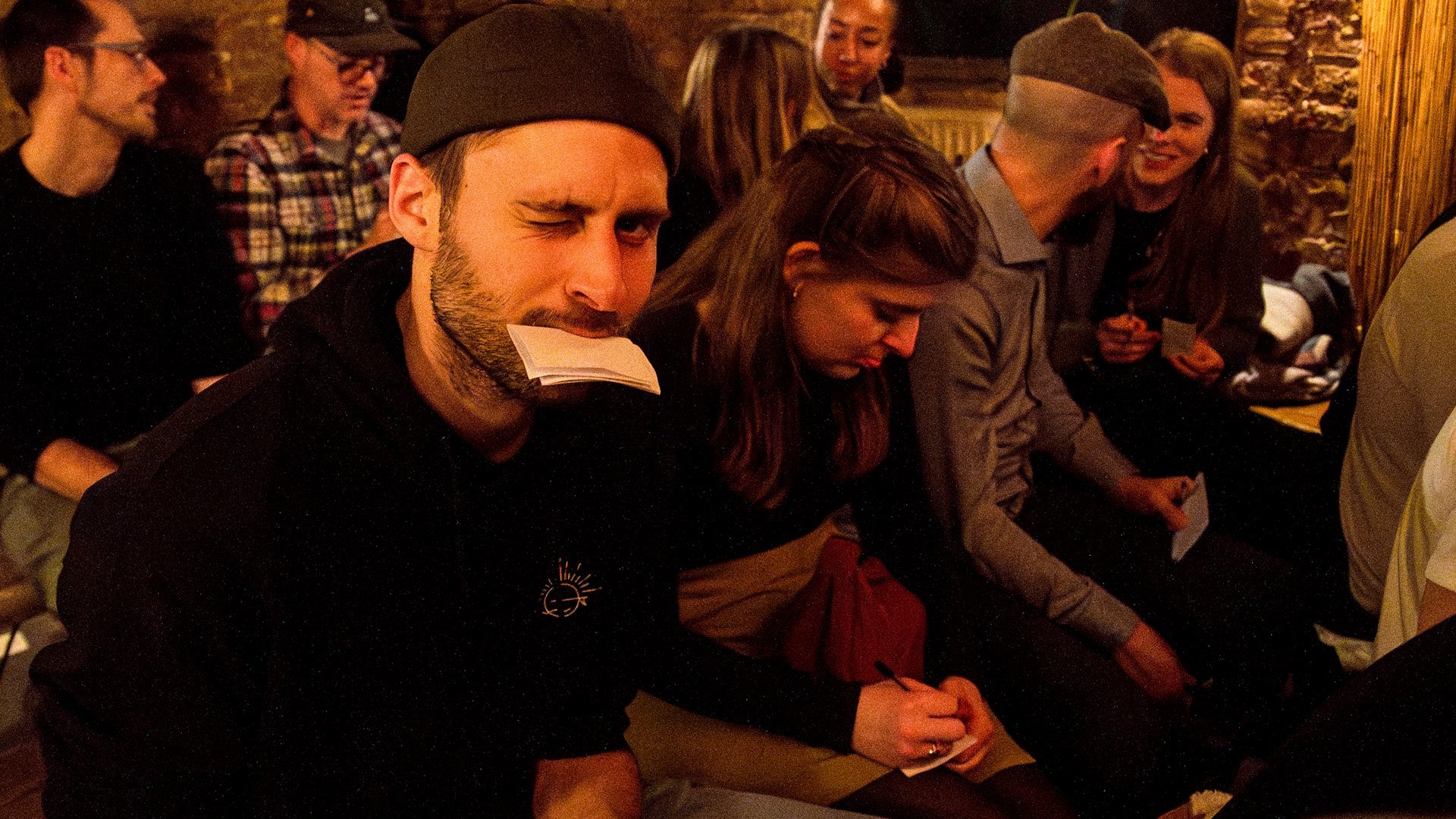 Audience members crowded close together write their darkest thoughts on paper notes at a Darkest Thoughts show in Berlin