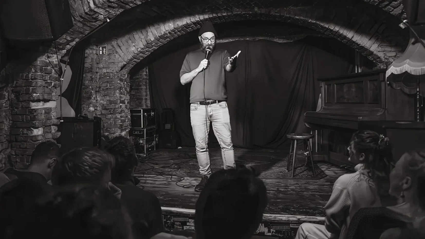 Black-and-white shot of comedian Ori Halevy performing stand-up under a brick arch at a Darkest Thoughts show in Berlin