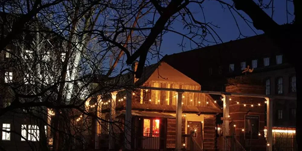 The Wilhelmshütte theater building glowing with warm fairy lights at night, seen through bare tree branches, in Berlin