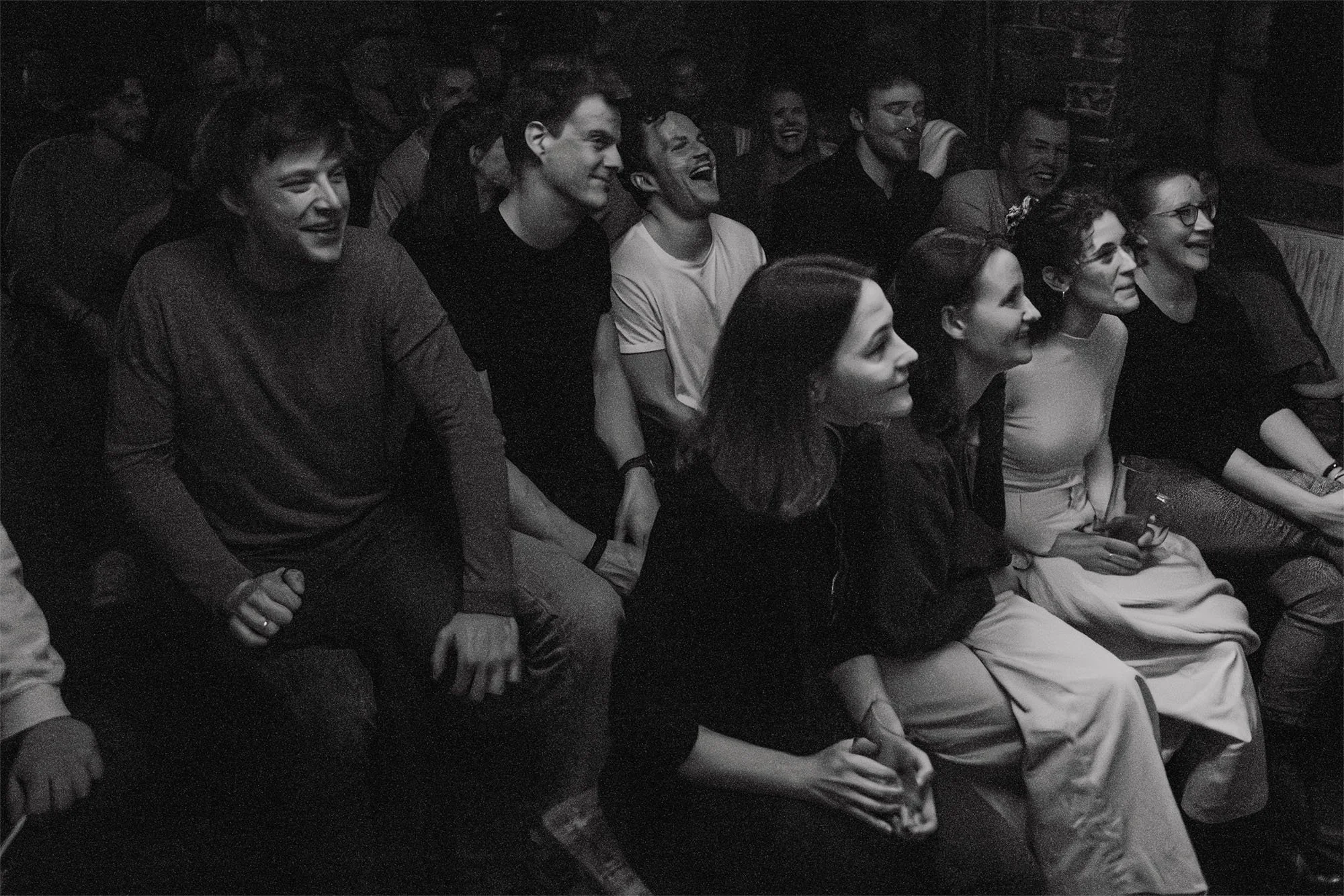 Black-and-white photo of audience members laughing at a comedy show