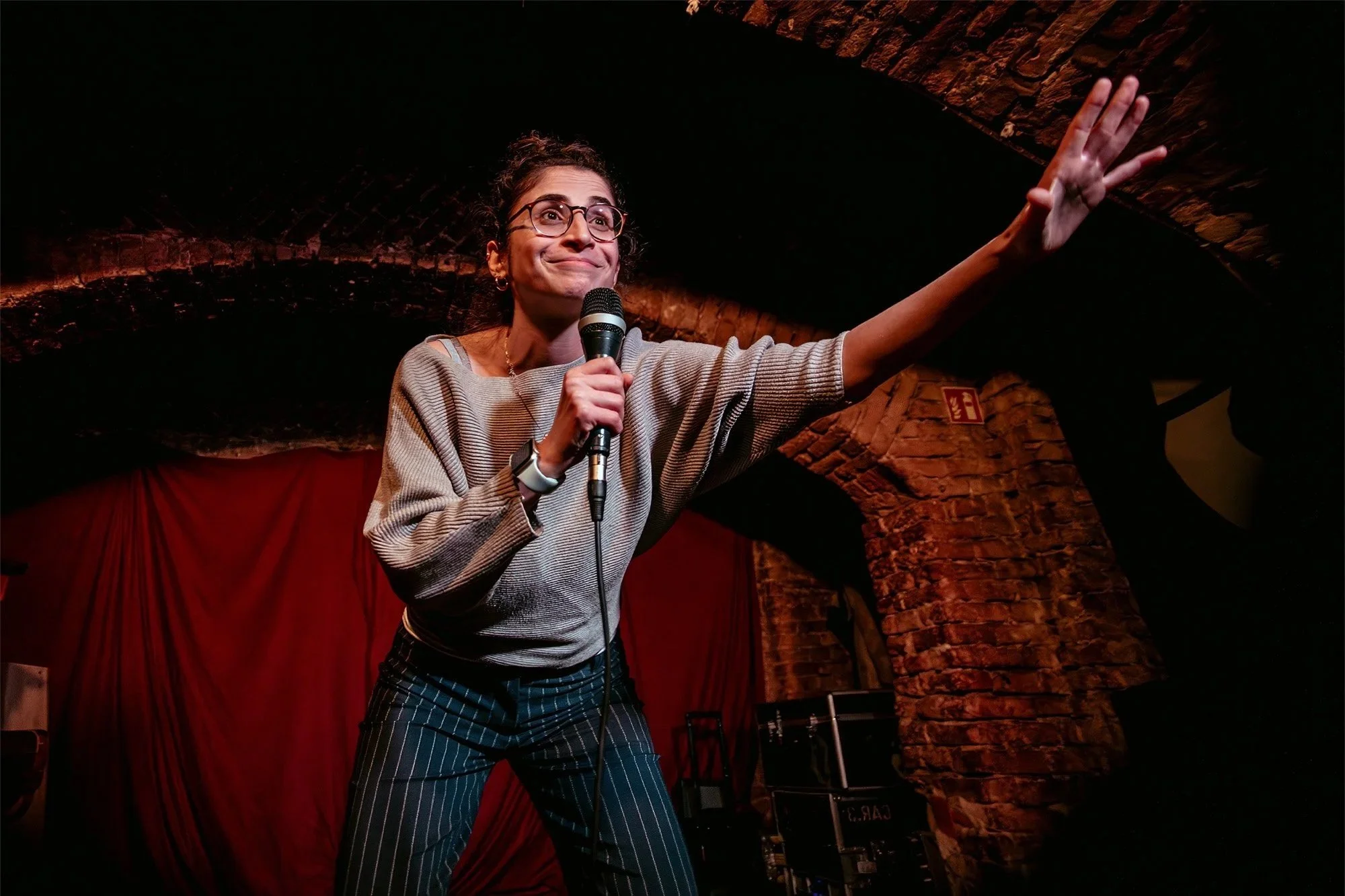 Female stand-up comedian with a microphone performing under a brick arch