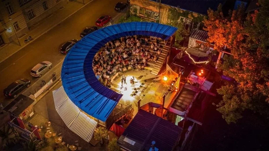 Aerial view of the open-air amphitheater at Monbijou Theater in Berlin, lit up at night with a seated audience