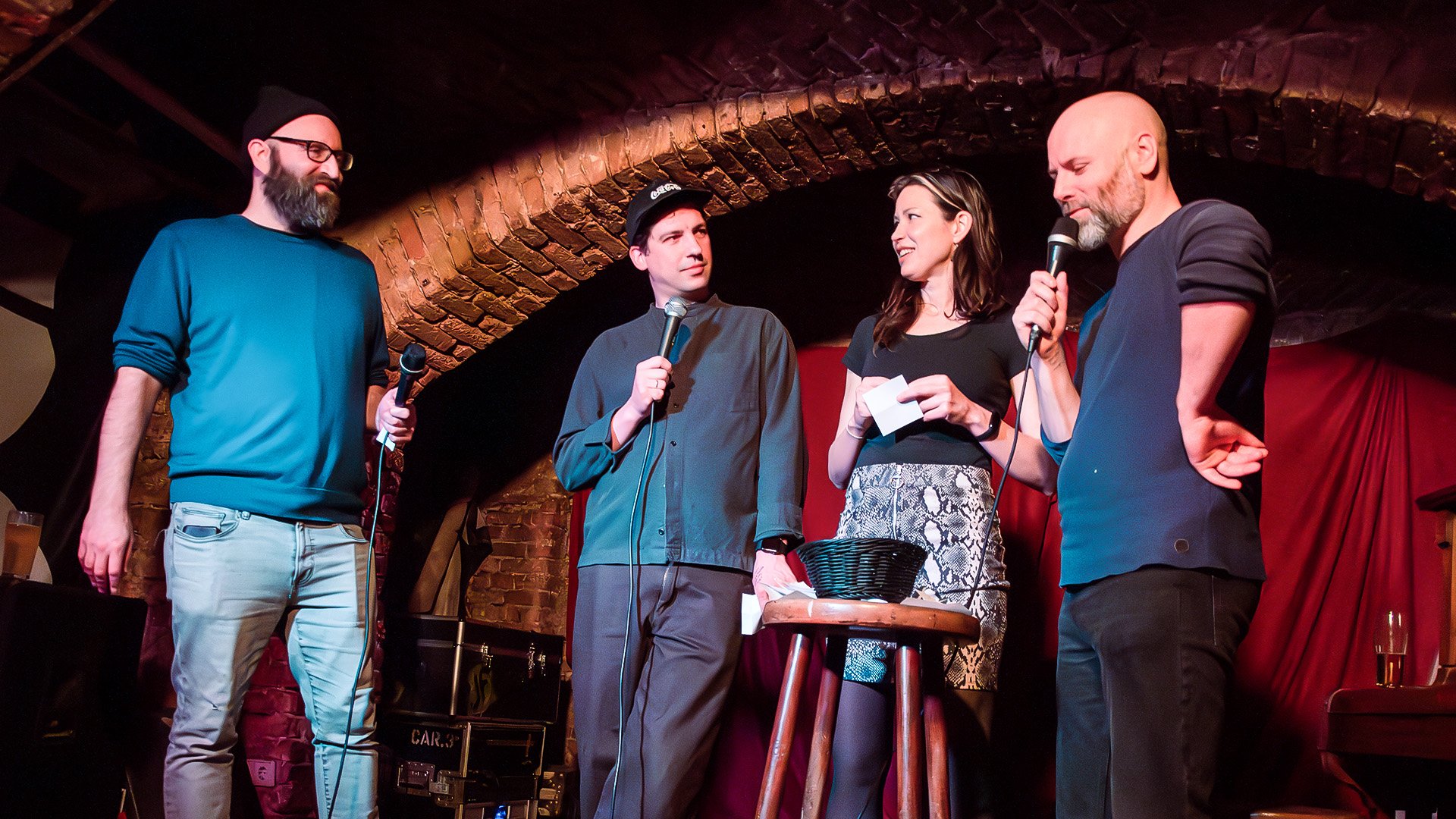 Ori Halevy, Brendan Hickey and two fellow comedians on stage under a brick arch, reading notes from the audience