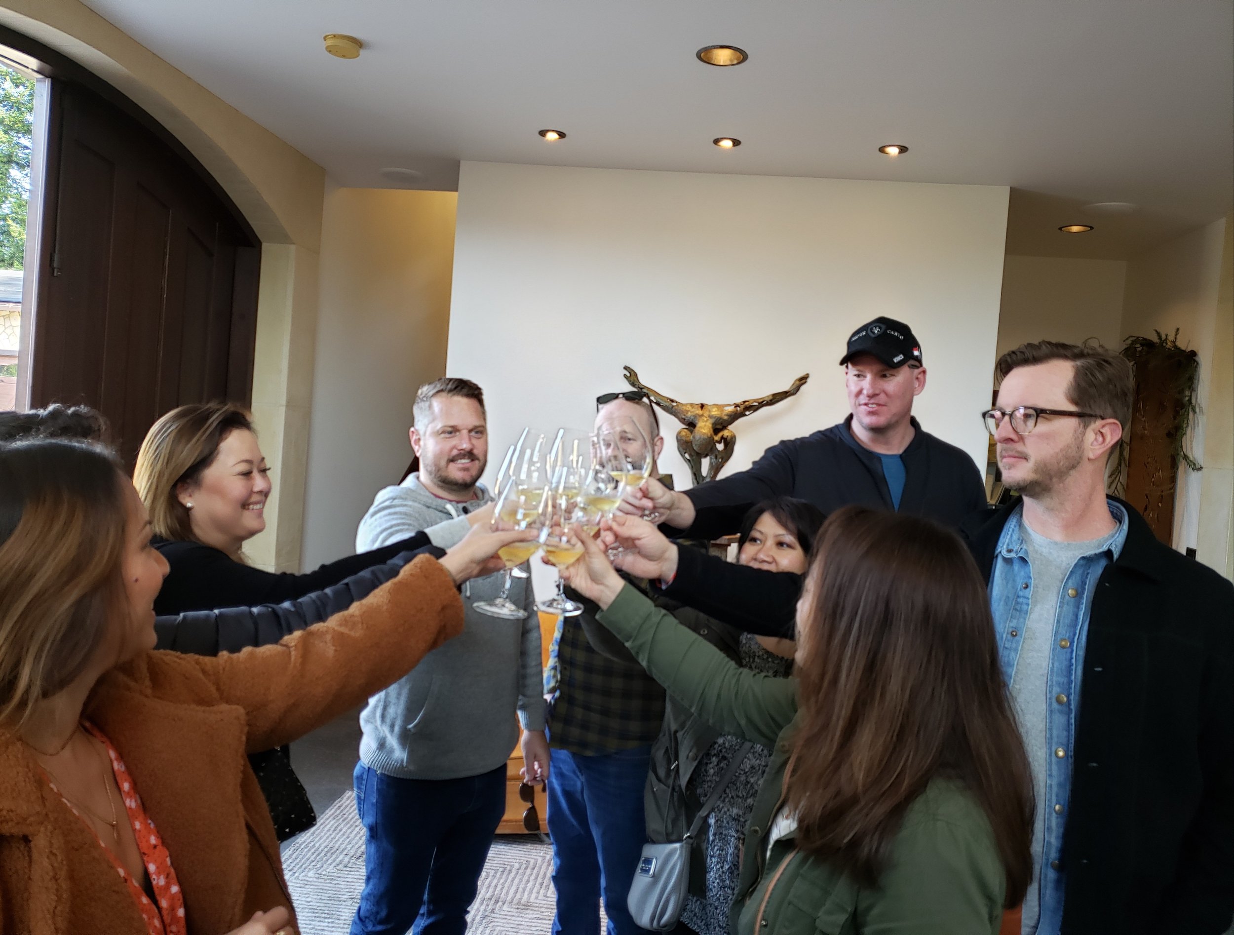 A group of people enjoying a toast with glasses of white wine in a cozy indoor setting.