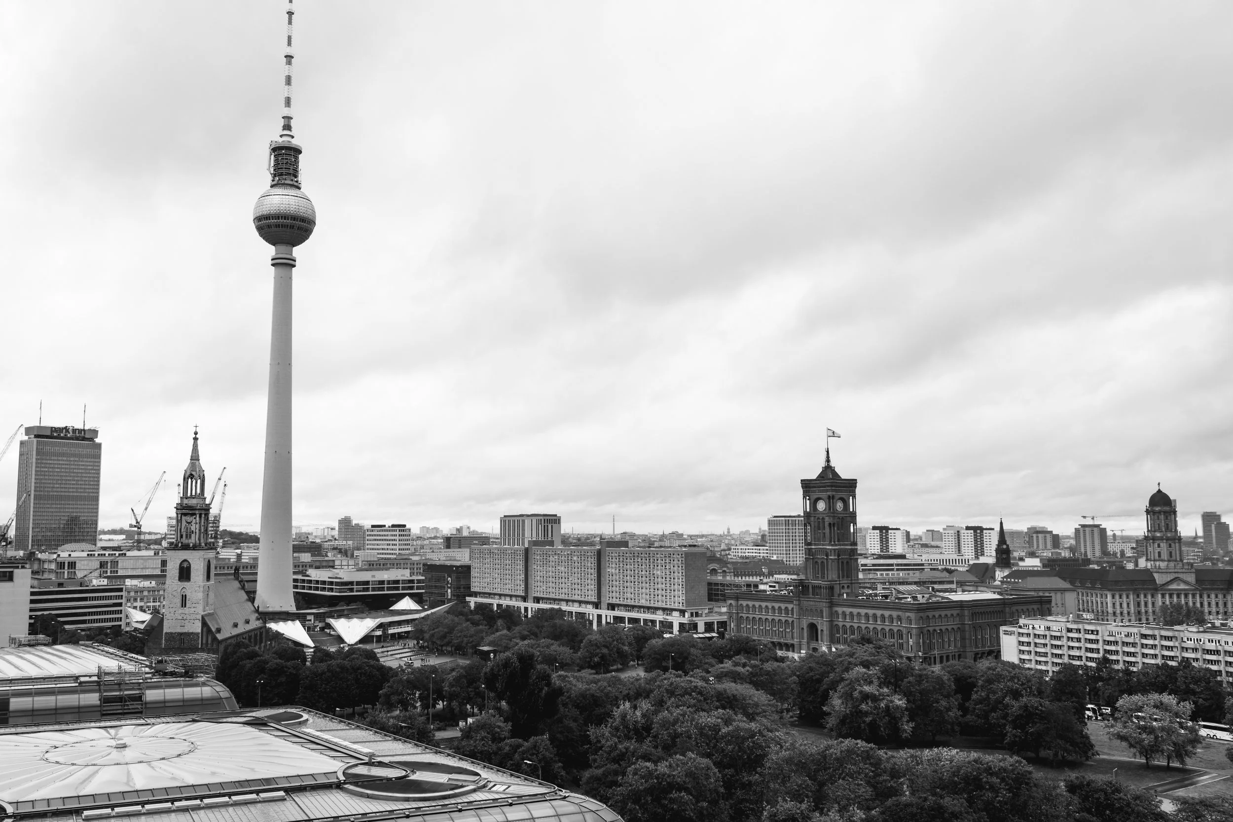Black and white cityscape featuring the Berlin TV Tower, historical buildings, and modern high-rises, with cloudy sky overhead.