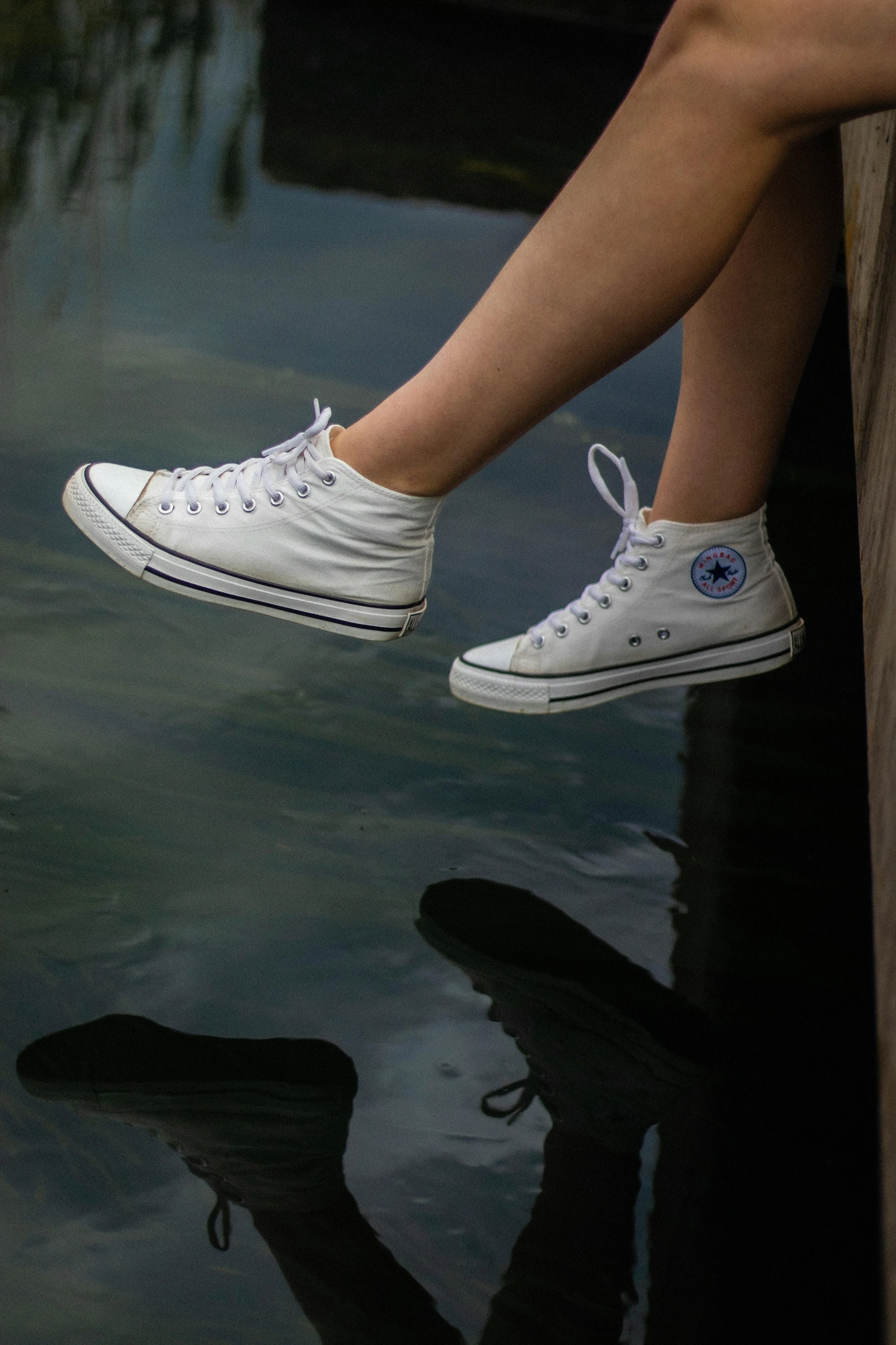 Pair of legs wearing white high-top sneakers, reflected in water