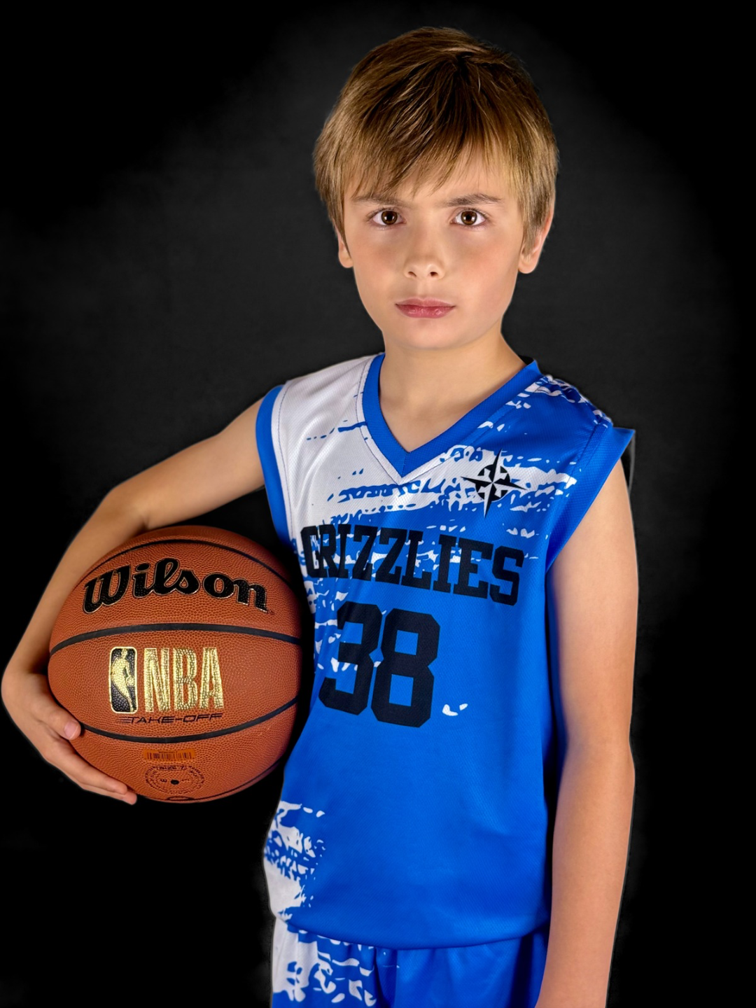 Young boy in a blue basketball jersey holding a basketball, against a dark background.