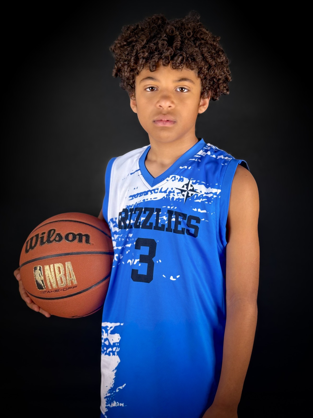 Young boy in a blue basketball uniform holding a basketball, standing against a black background.
