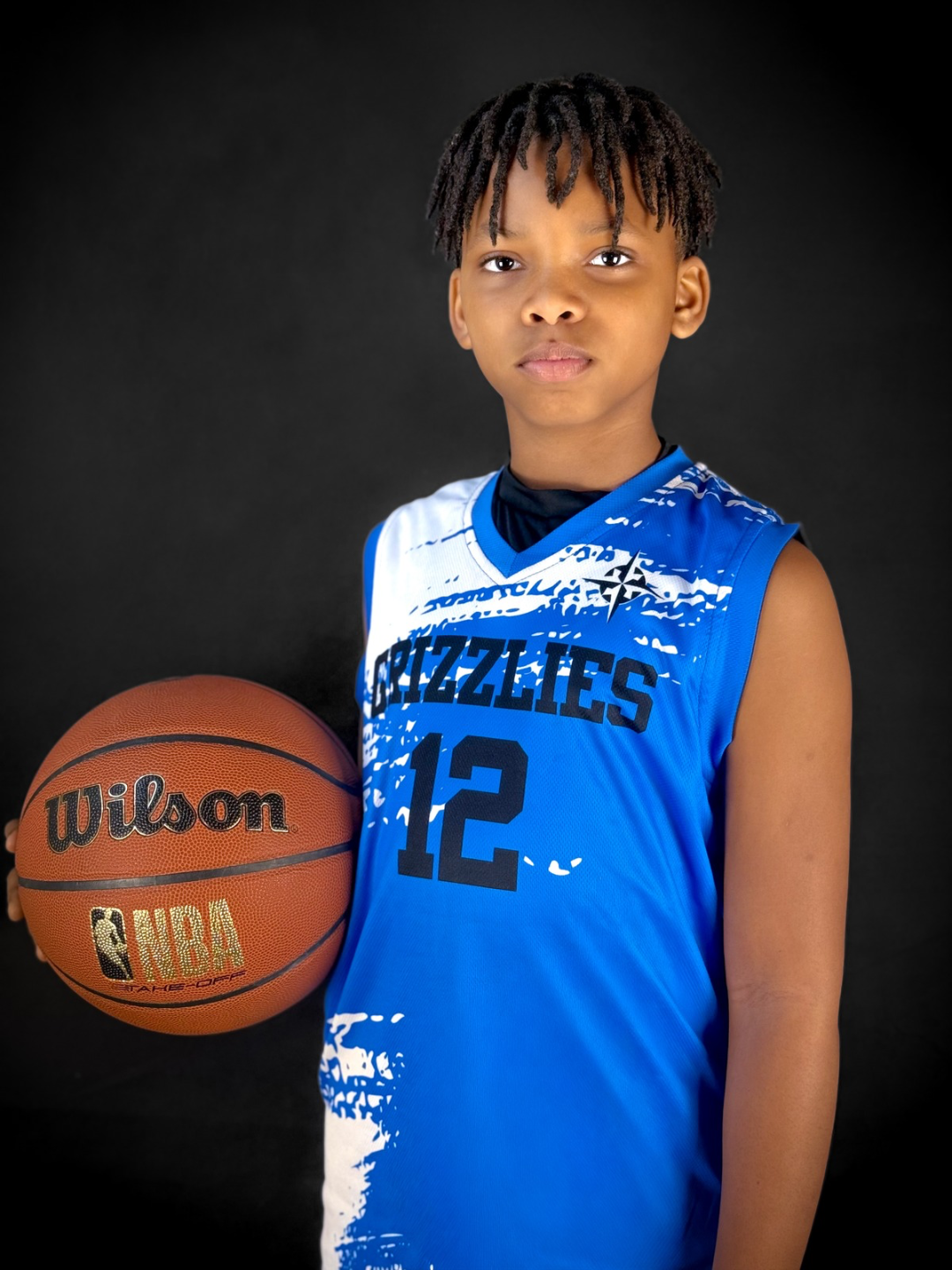Young boy in a blue Memphis Grizzlies basketball jersey holding a Wilson NBA basketball against a black background.