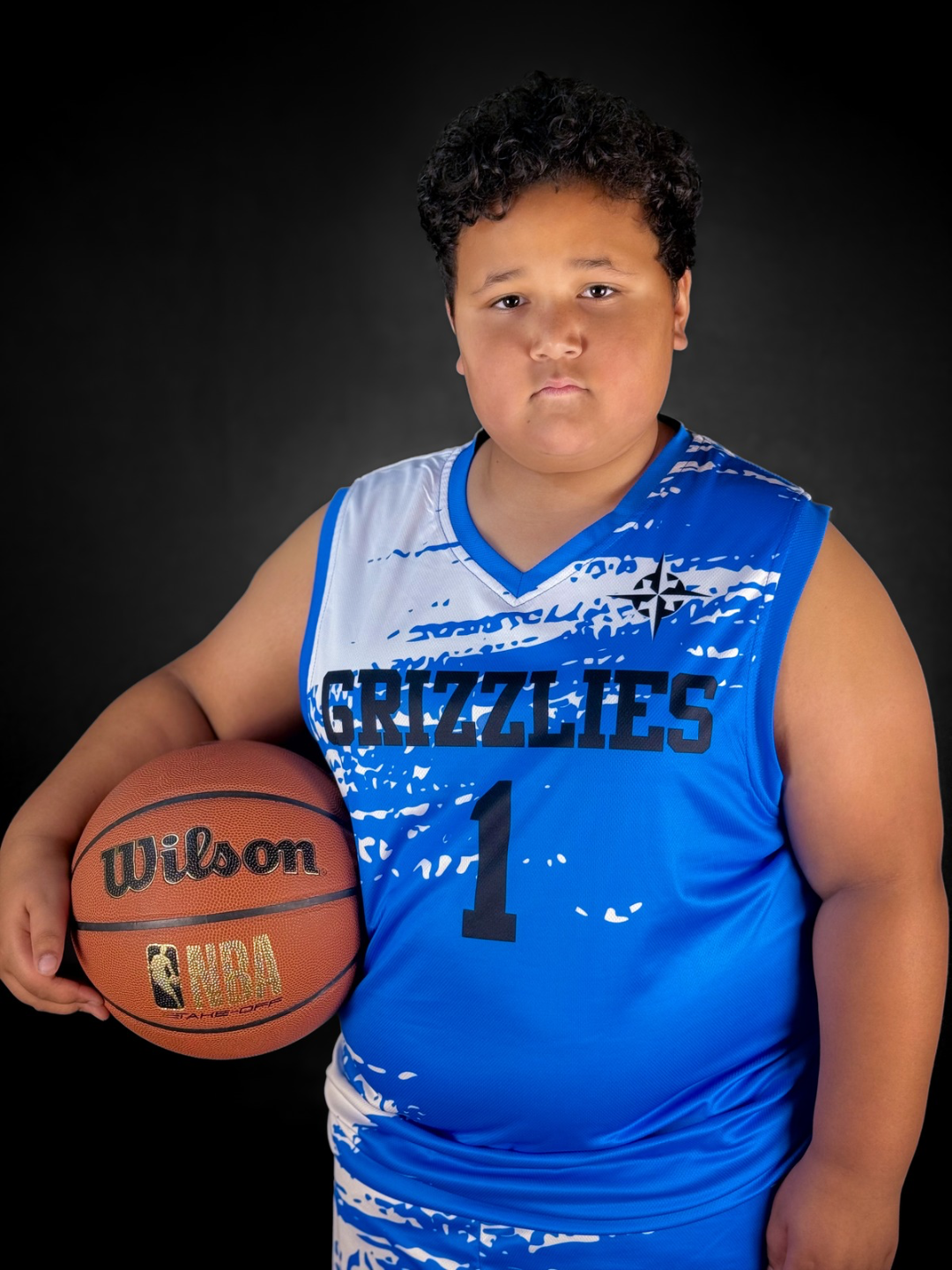 Young boy in a blue Memphis Grizzlies basketball uniform holding a Wilson NBA basketball against a black background.