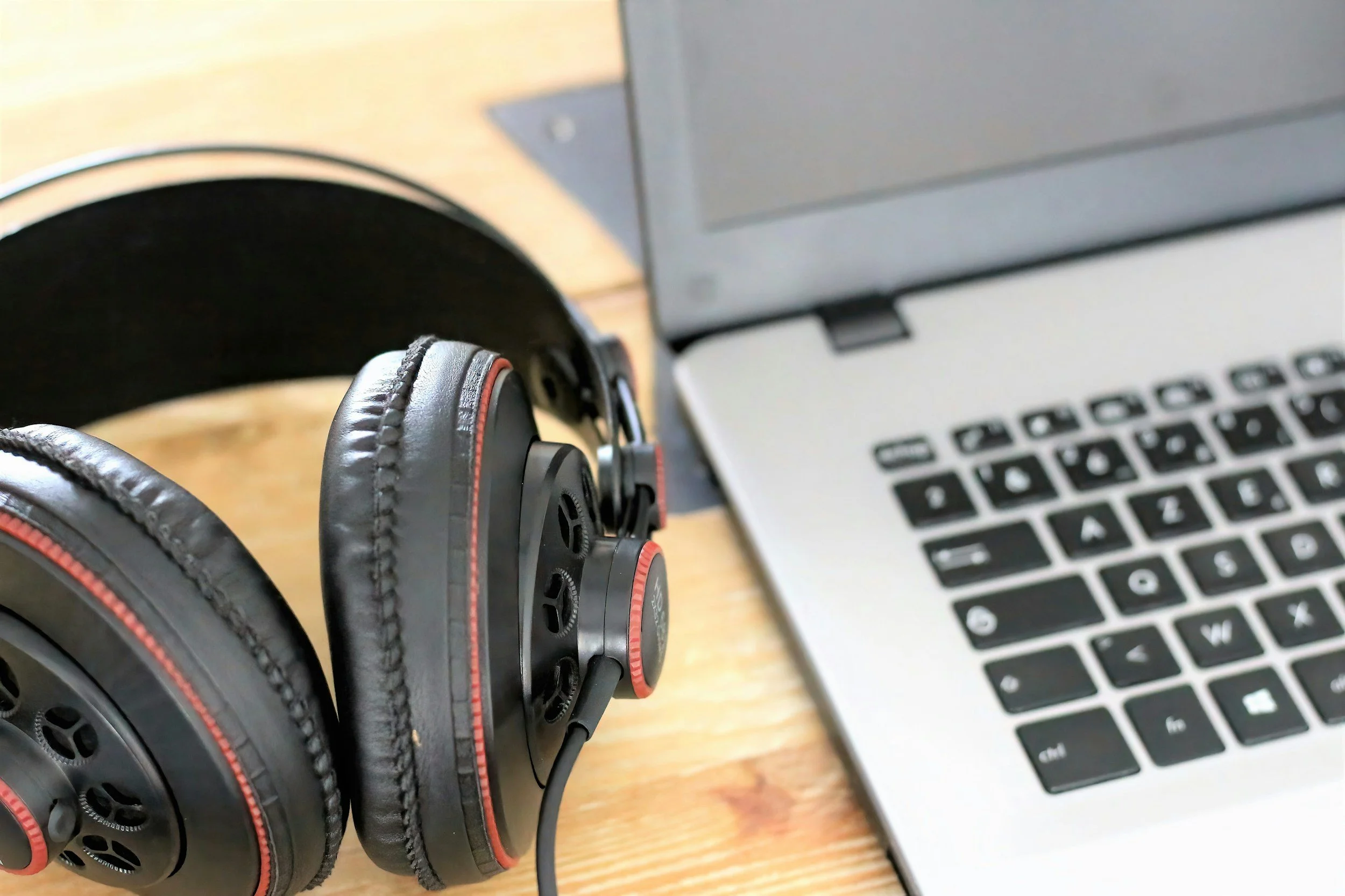 Black over-ear headphones and a silver laptop on a wooden surface.