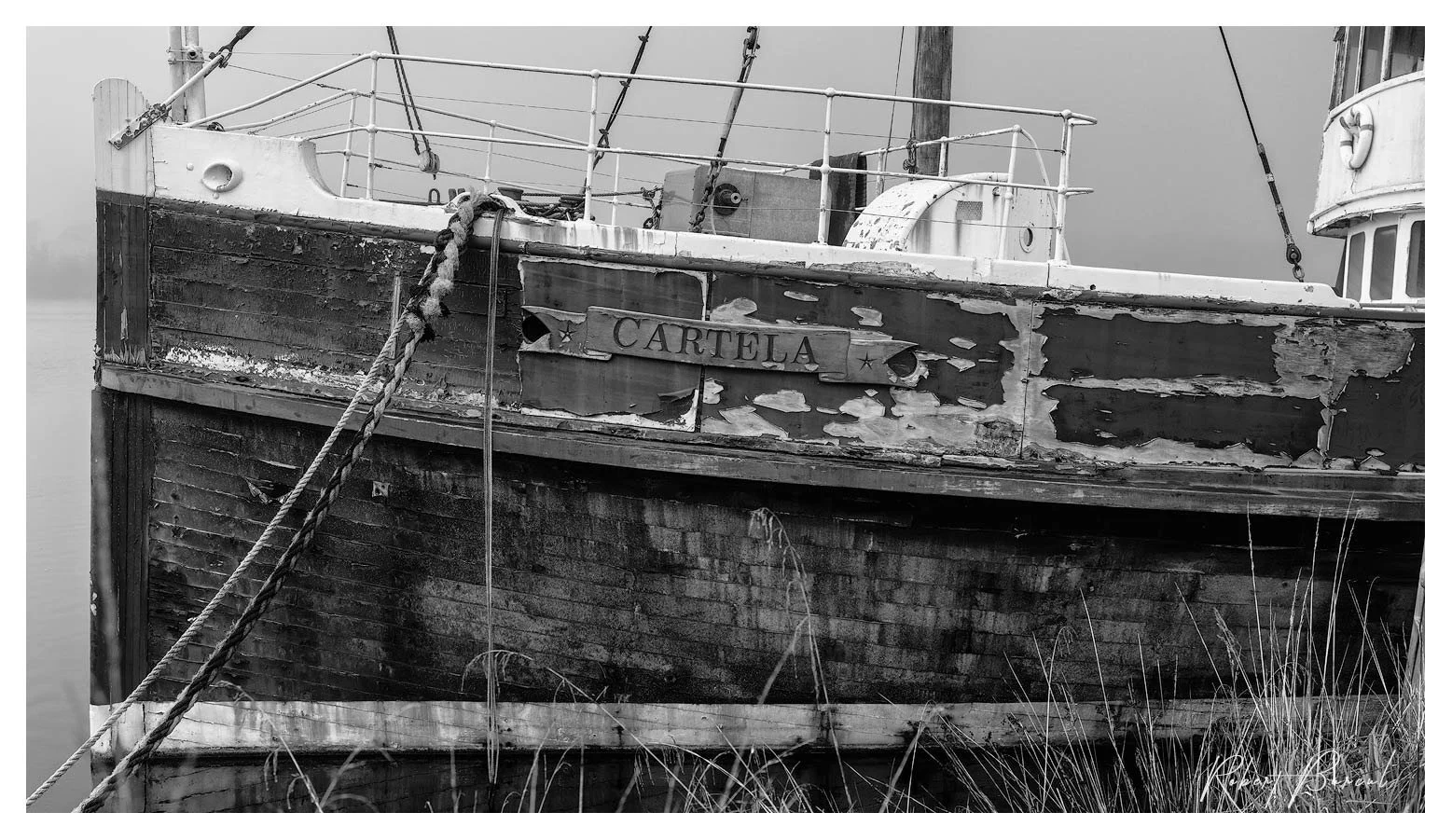 Black and white close view of a weathered boat hull, showing worn planks and a chain hanging across its side.