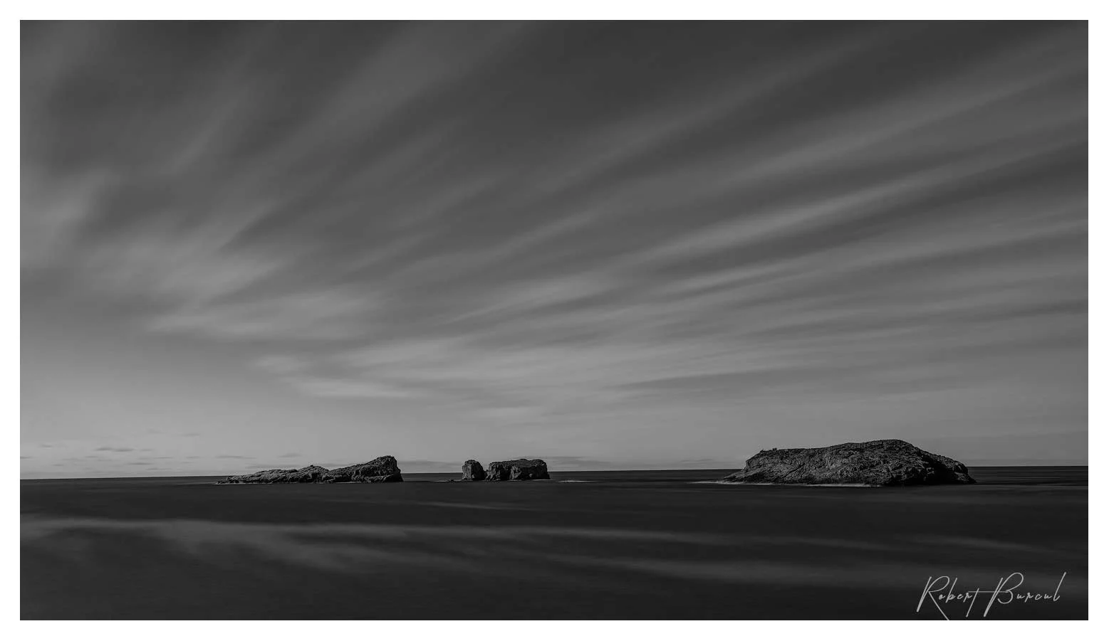 Black and white seascape with distant island shapes along the horizon  and streaking clouds  above the dark ocean.