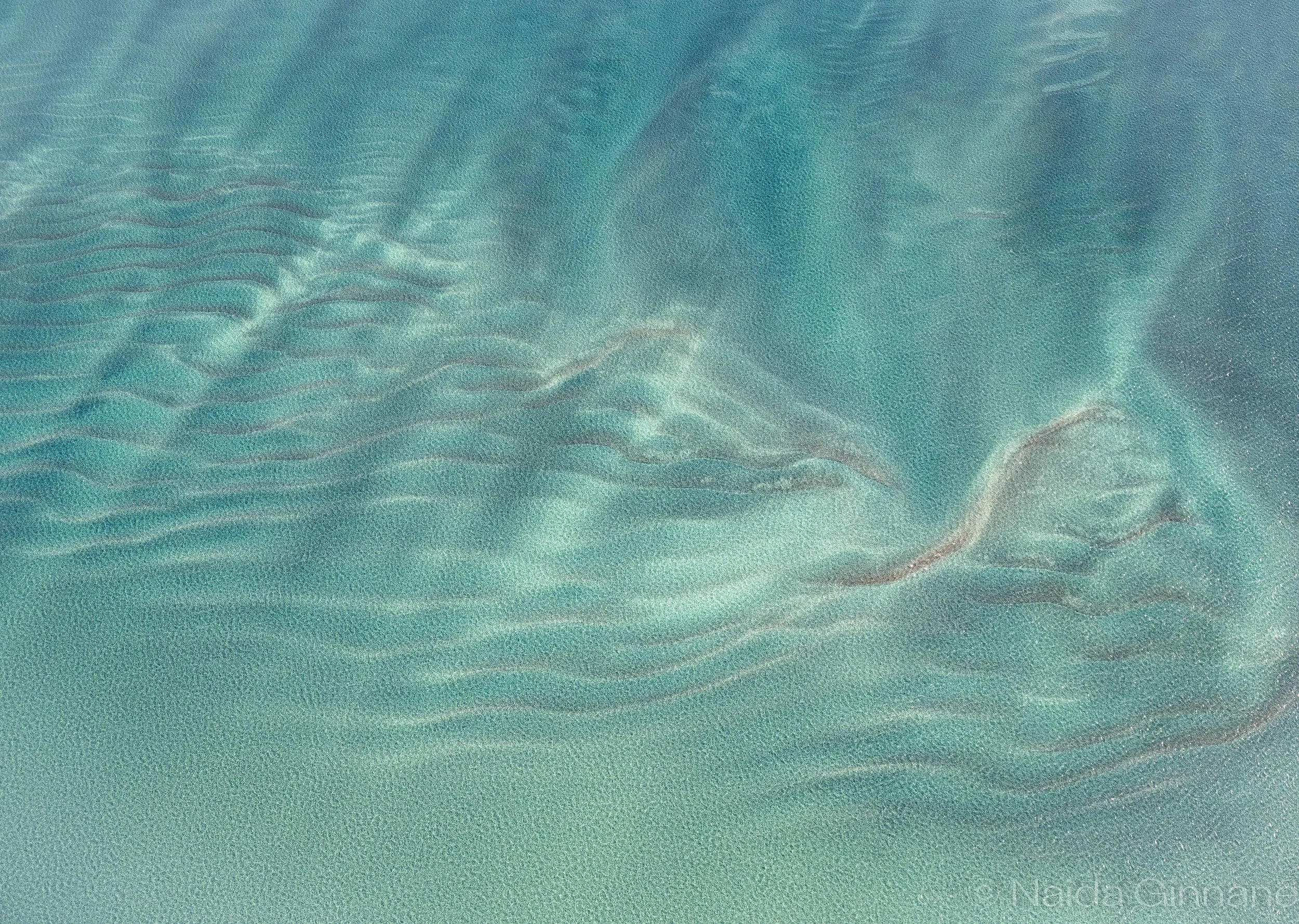 Shallow Breath — Abstract aerial photograph  in soft turquoise and pale sand tones, rippling wave patterns; calming coastal palette suited to spa, bathroom, or serene living spaces.