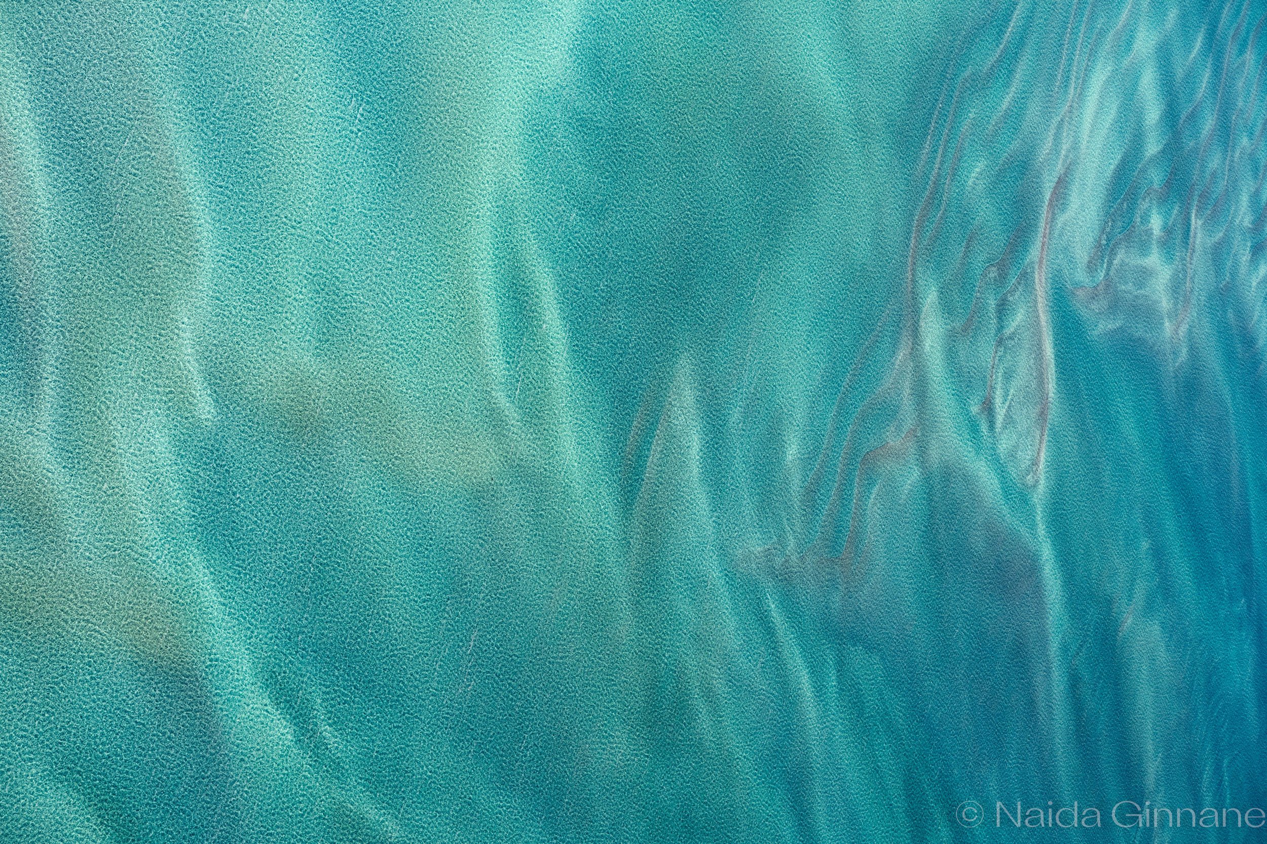 Shallow Sigh — Abstract aerial photograph  in teal and turquoise tones, a darker current cutting through rippled water; fluid, soothing piece for coastal or contemporary interiors.