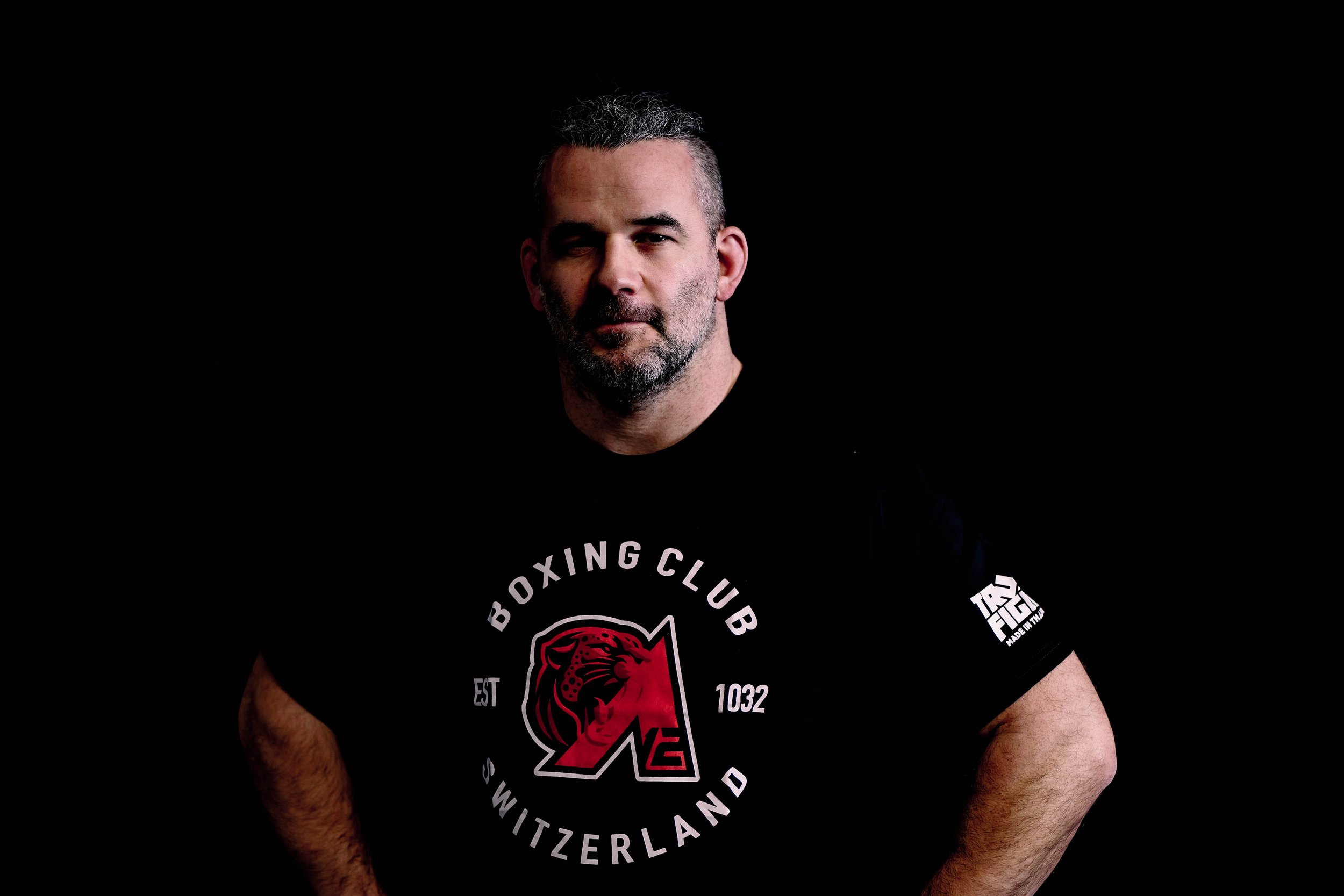 David, le coach Grappling à Romanel-sur-Lausanne, Un homme avec une barbe portant un t-shirt noir avec un logo du Boxing Club Switzerland et le texte "est 1032" et un lion rouge
