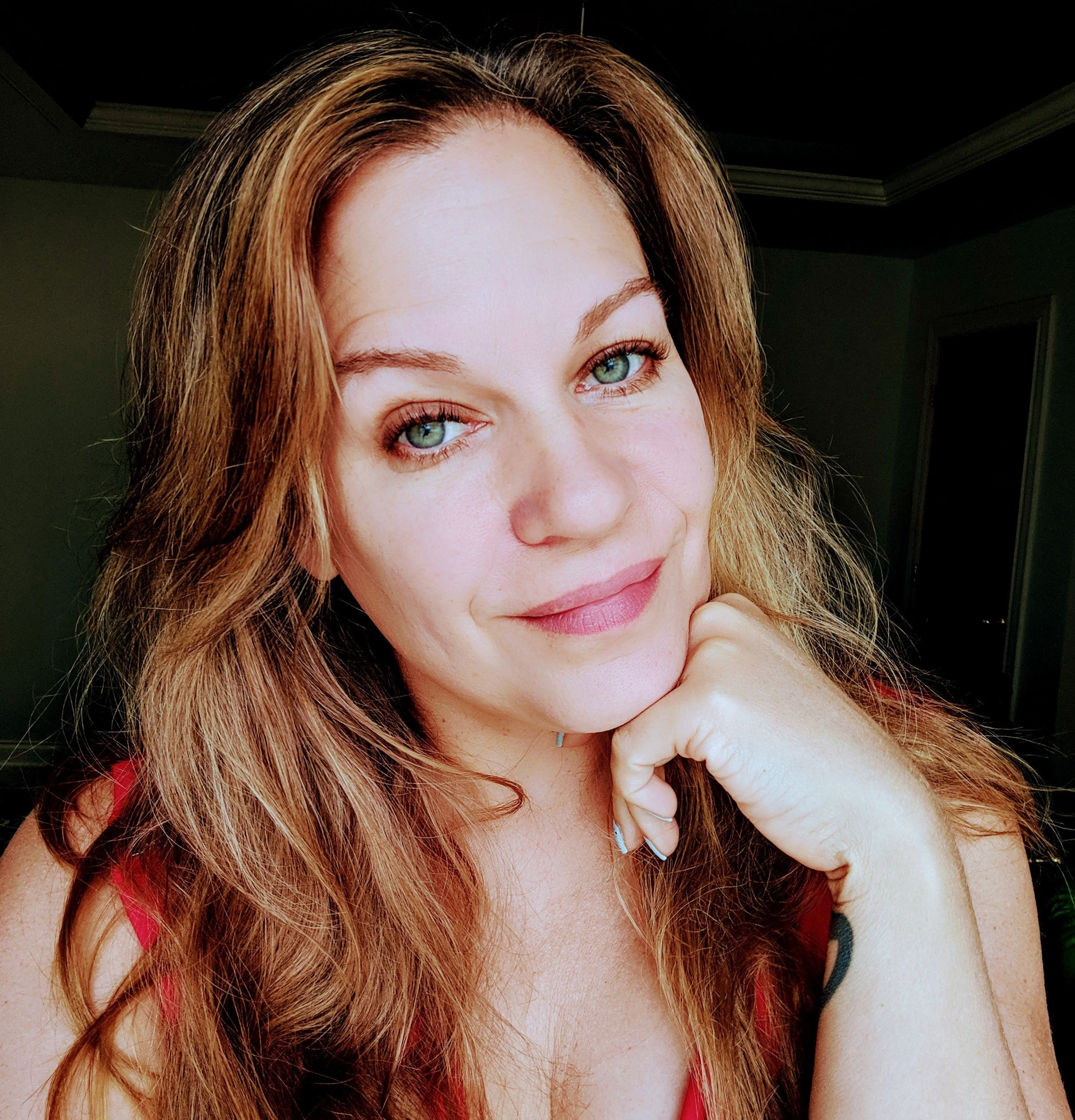 Close-up of a woman with long, wavy hair and green eyes, resting her chin on her hand.