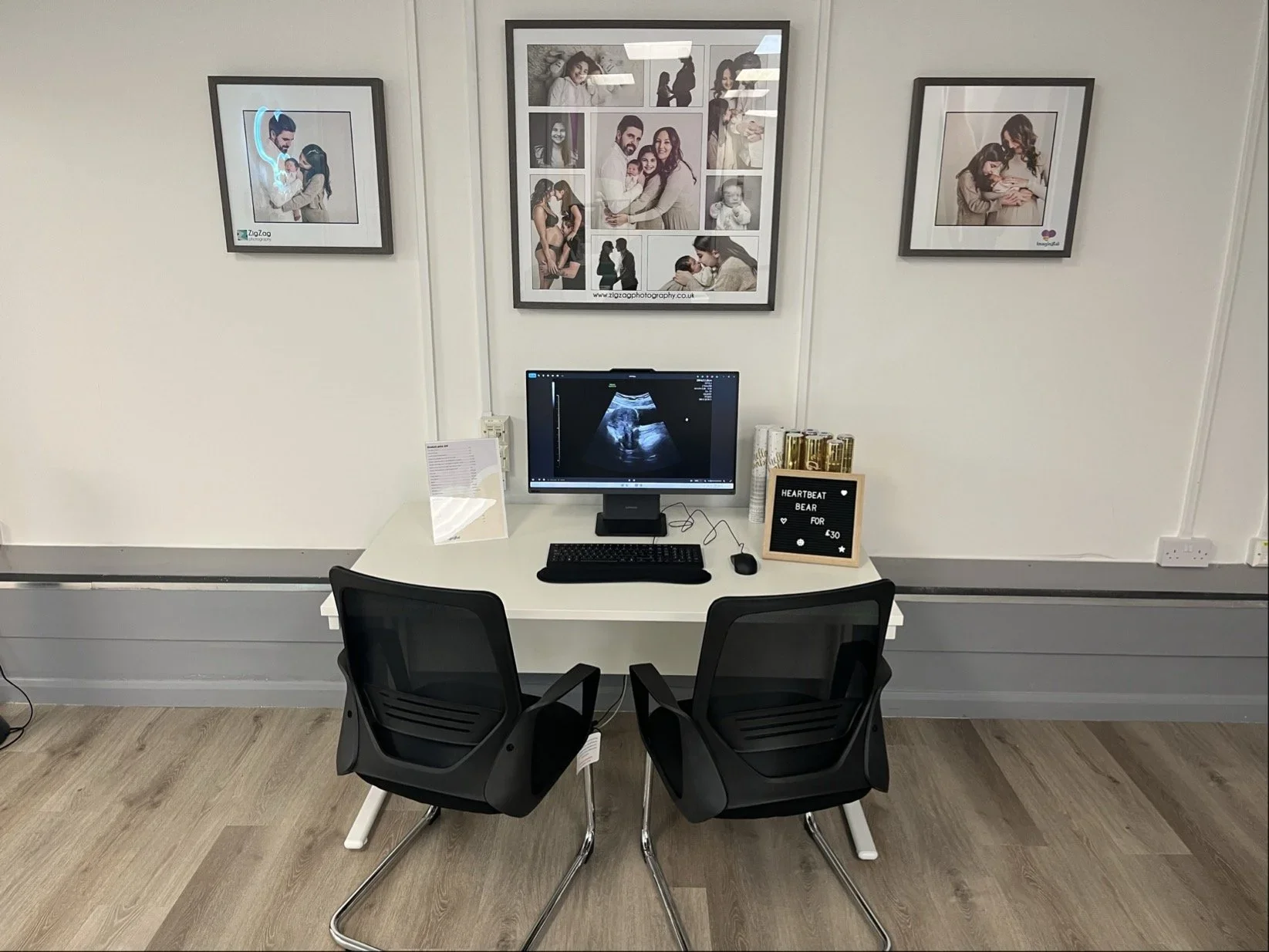 Ultrasound viewing area at Imaginatal private clinic with a desk setup, baby scan images on the monitor, seating for clients, and framed maternity photos on the wall.