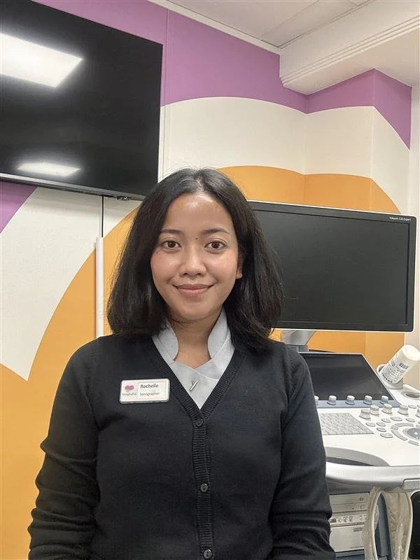 Rochelle, sonographer at Imaginatal, standing in a clinic room beside an ultrasound machine.