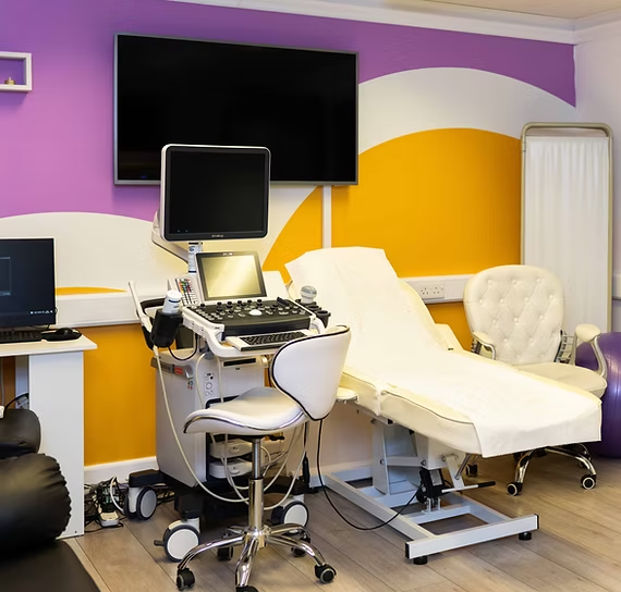 Medical examination room with ultrasound equipment, monitor, adjustable bed, and colorful walls.