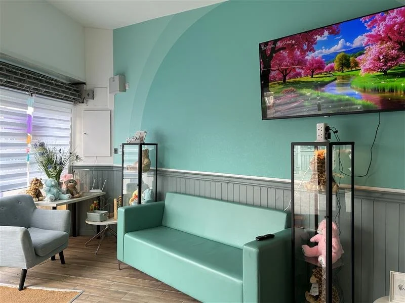 Waiting area at the clinic with a teal sofa, display cabinets of heart beat bears, and a wall-mounted TV.