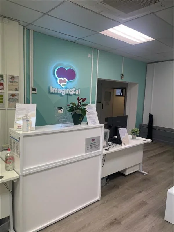 Imaginatal Leicester reception area with a bright teal feature wall, welcoming front desk, and calm, modern space where clients arrive for private ultrasound and baby scans.