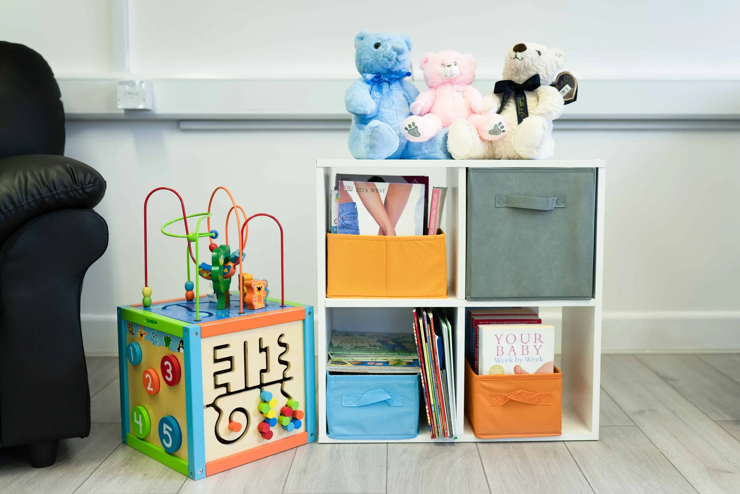 Children's play area with educational toys, storage cubbies, books, and teddy bears in the waiting room of an Imaginatal pregnancy ultrasound clinic.