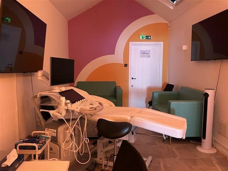 Ultrasound scan room at Imaginatal Cardiff with a medical scanning bed, ultrasound machine, two wall-mounted screens, and comfortable seating.
