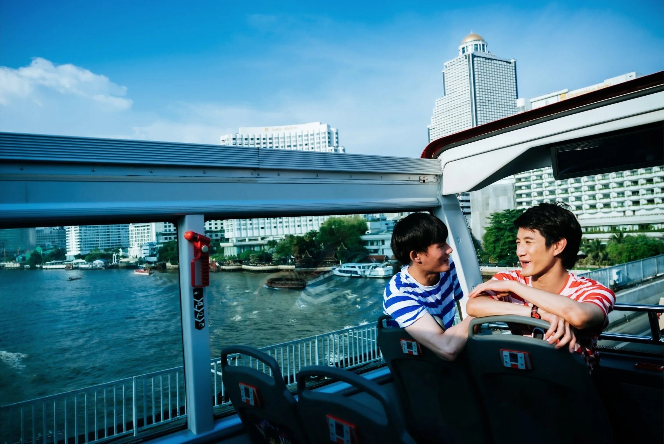 Queer Asian men sitting in a boat overlooking a body of water, smiling and talking to each other.
