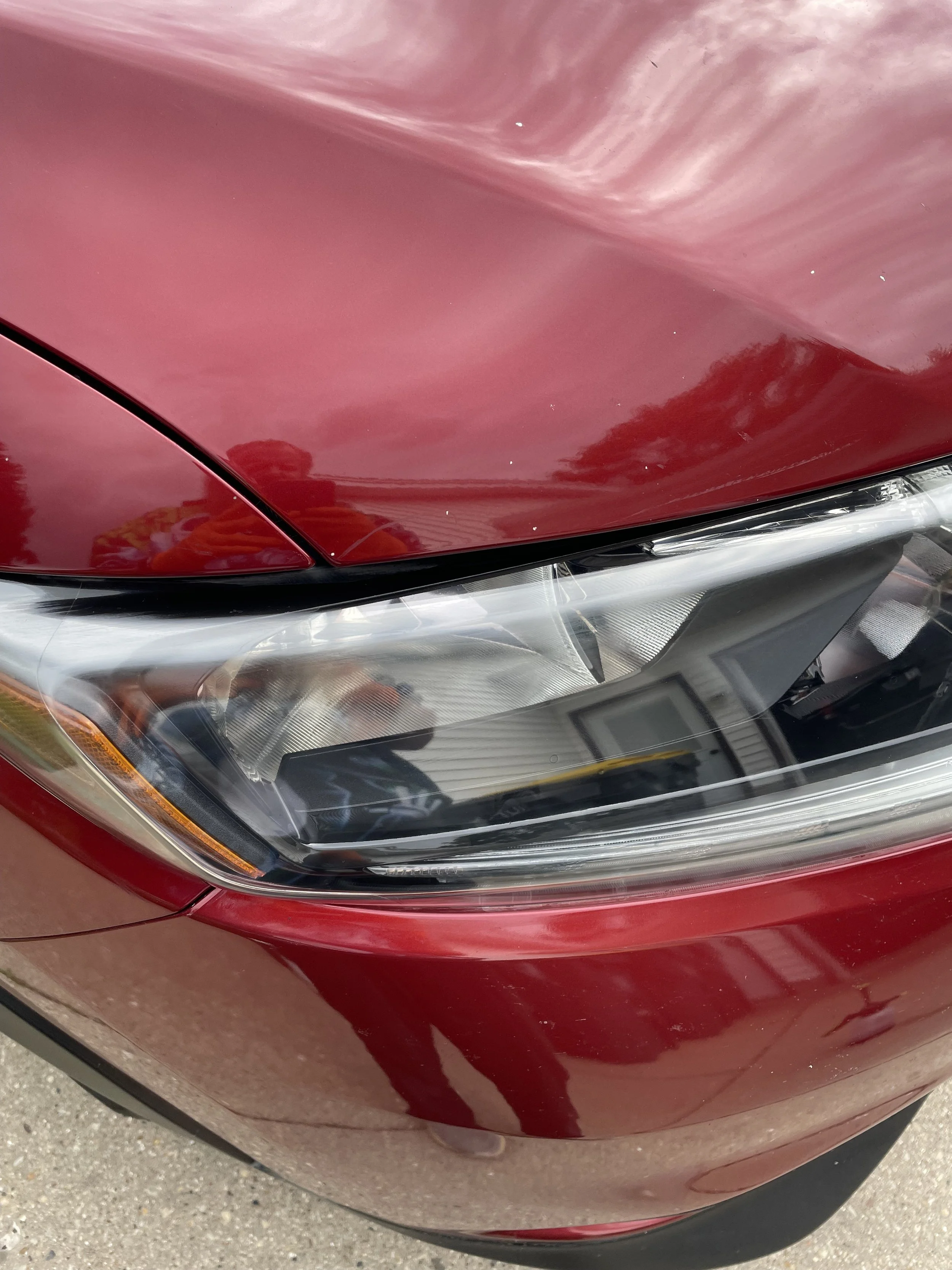 Close-up of a red car's front headlight and part of the hood.