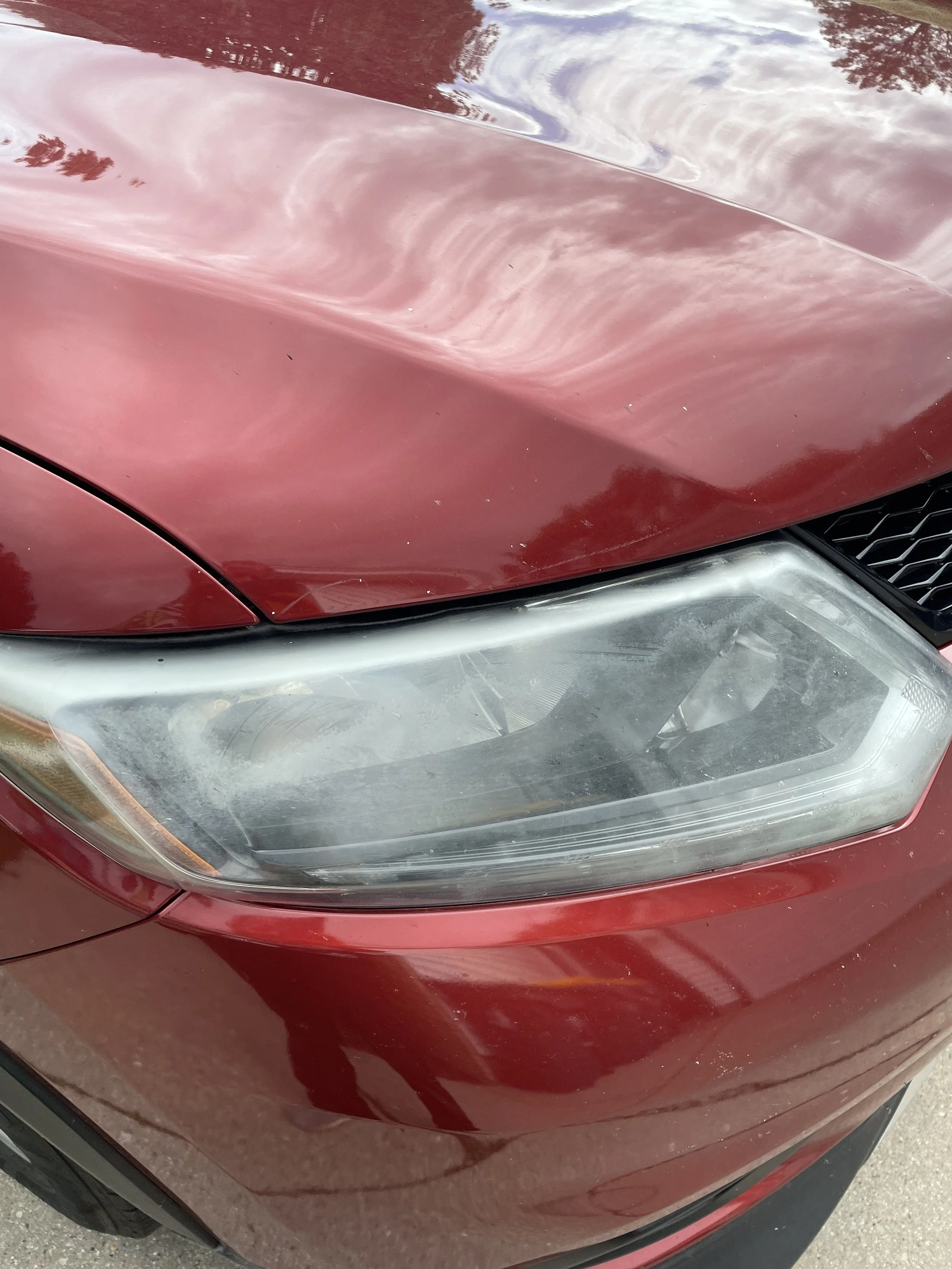 The front of a red car showing the hood, headlight, and part of the front grille.