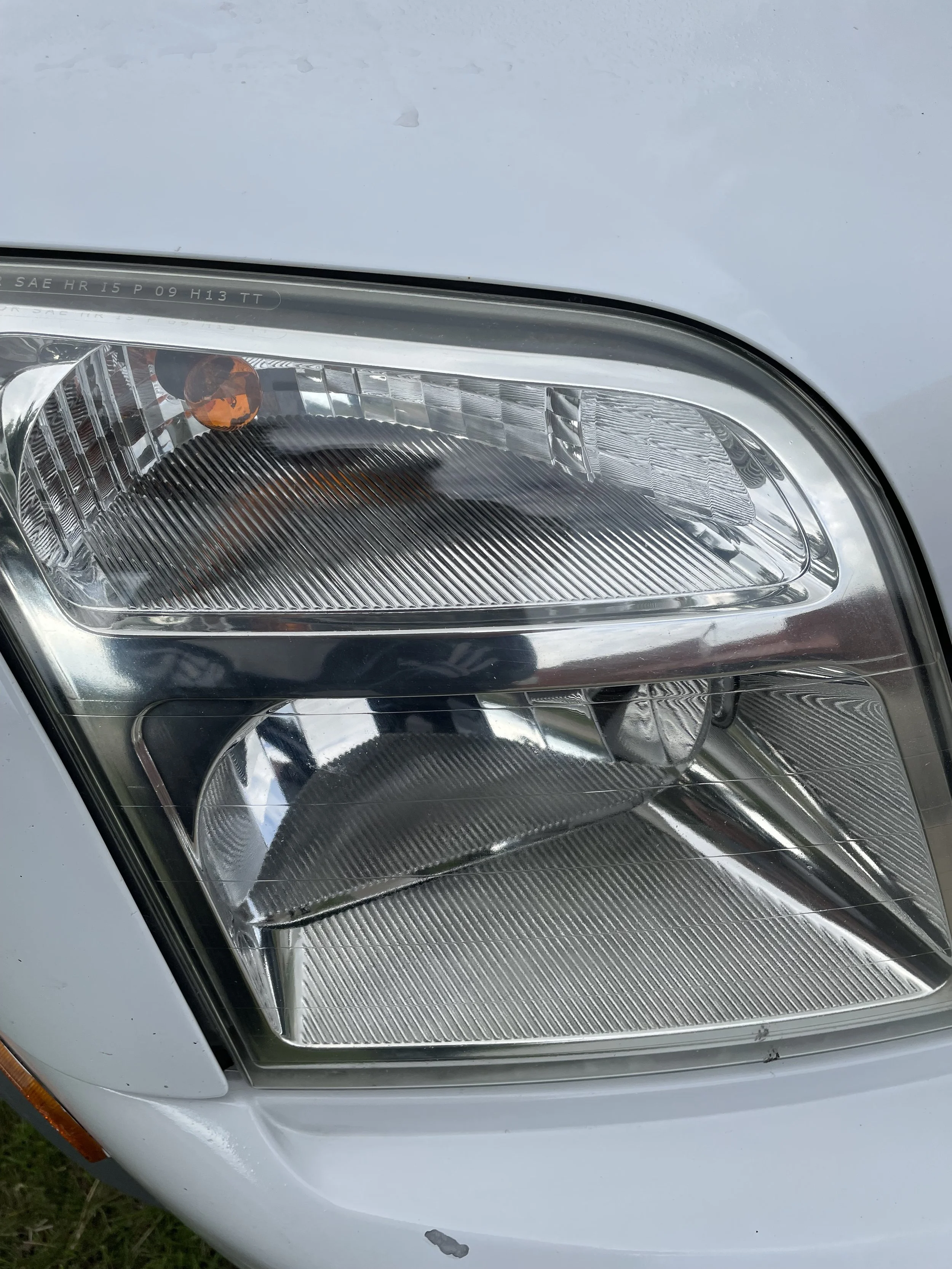 Close-up of a car headlight on a white vehicle, showing the headlight's clear plastic cover and internal reflective surfaces.