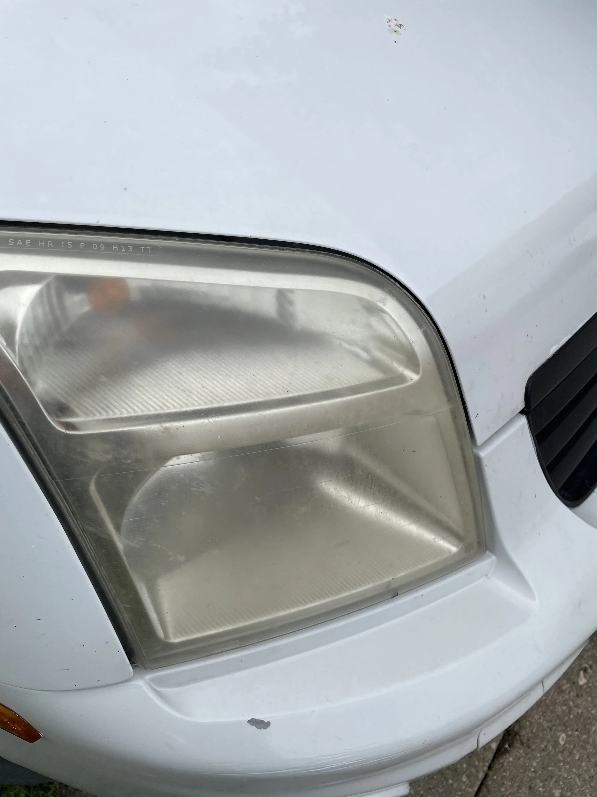 Close-up of a car's front headlight and part of the hood, which has some dirt and paint chips.