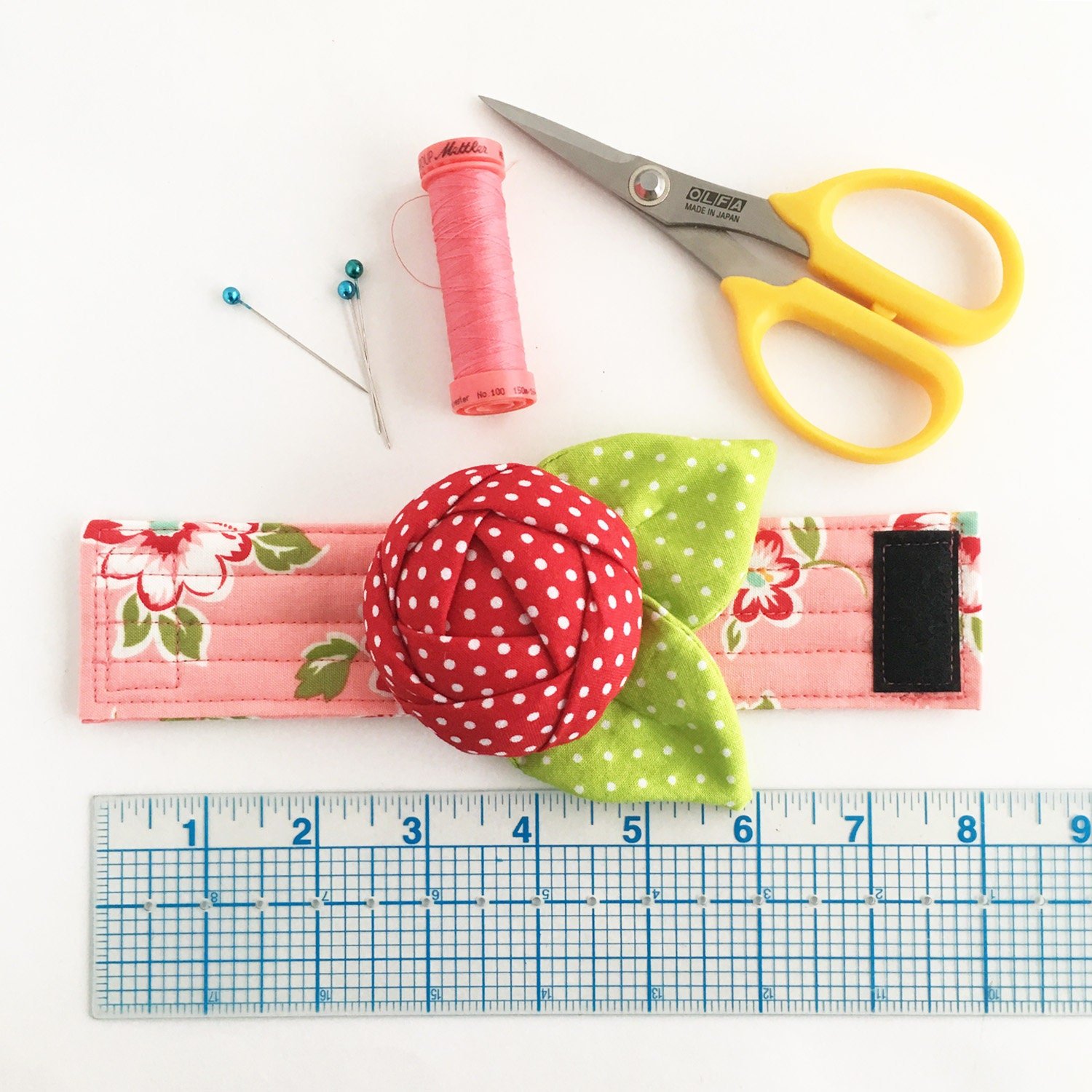 Pin cushion cuff with ruler and sewing notions for size reference.